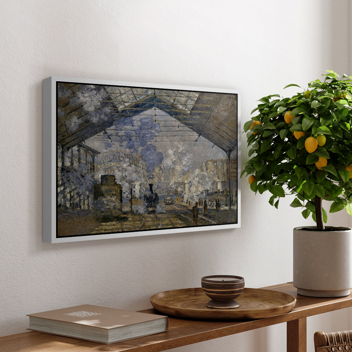 The Gare Saint-Lazare, 1877 by Claude Monet, presented in a white floater framed canvas featuring a train station interior filled with steam and locomotives under iron structure, displayed above a hallway console table.