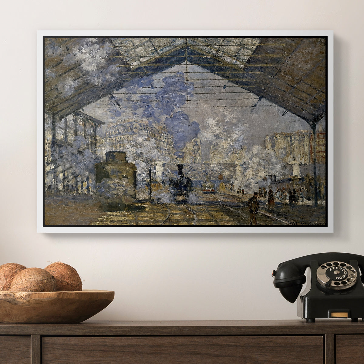 The Gare Saint-Lazare, 1877 by Claude Monet in a white floater framed canvas displayed above a console table in a hallway, featuring a bustling transport hub with trains beneath glass roof.