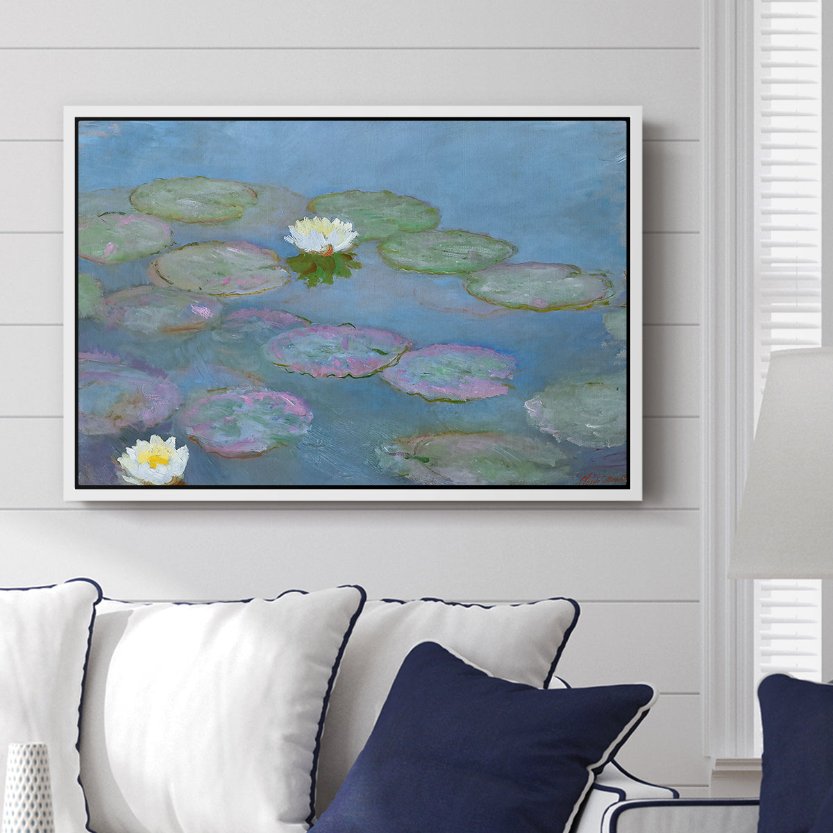 Water Lilies (Nymphéas), 1897-1899 by Claude Monet displayed above a sofa in a living room in a white floater frame, featuring an impressionist pond scene with lily pads and soft reflections.