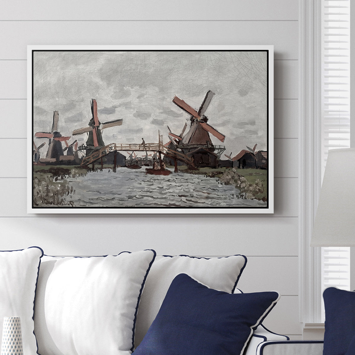 Windmills near Zaandam, 1871 by Claude Monet displayed above a sofa in a living room in a white floater frame, featuring an impressionist view of Dutch windmills along riverbank.
