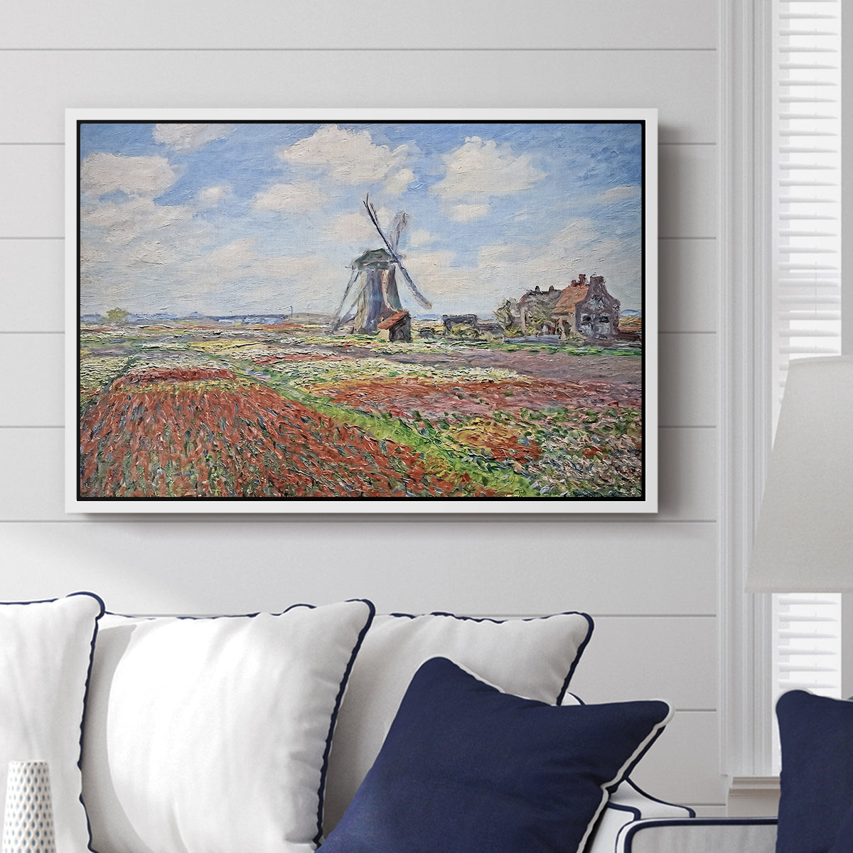 Tulip Fields with the Rijnsburg Windmill, 1886 by Claude Monet displayed above a sofa in a living room in a white floater frame, featuring a vibrant agricultural landscape with flowers and windmill.