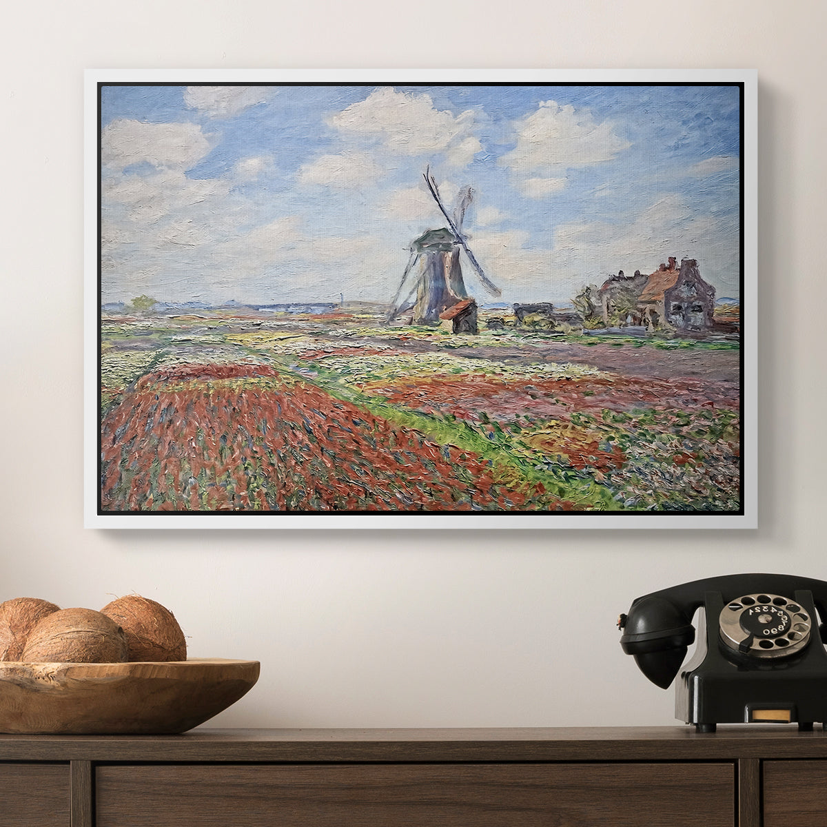 Tulip Fields with the Rijnsburg Windmill, 1886 by Claude Monet in a white floater framed canvas displayed above a console table in a hallway, featuring a rural scene with patterned rows of flowers and windmill.