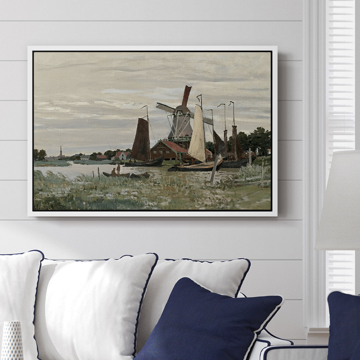 Windmill at Zaandam, 1871 by Claude Monet displayed above a sofa in a living room in a white floater frame, featuring an impressionist depiction of windmill near riverbank.