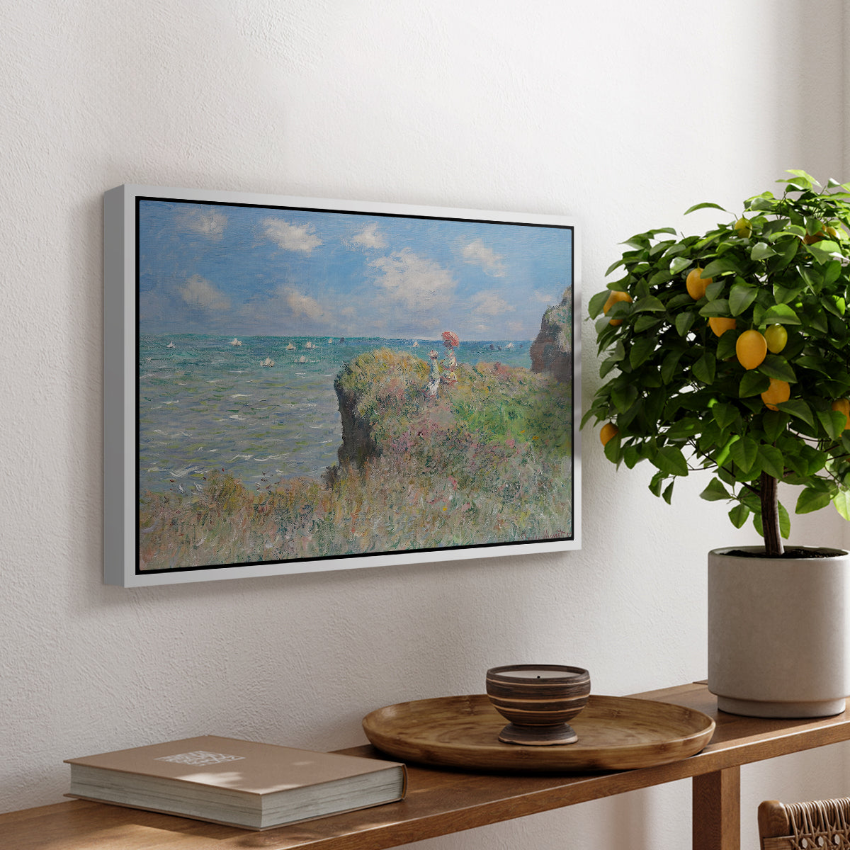 The Cliff Walk at Pourville, 1882 by Claude Monet, presented in a white floater framed canvas featuring figures walking along coastal cliff path overlooking ocean and sky, displayed above a hallway console table.