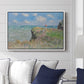 The Cliff Walk at Pourville, 1882 by Claude Monet displayed above a sofa in a living room in a white floater frame, featuring an impressionist seaside landscape with people strolling above water.