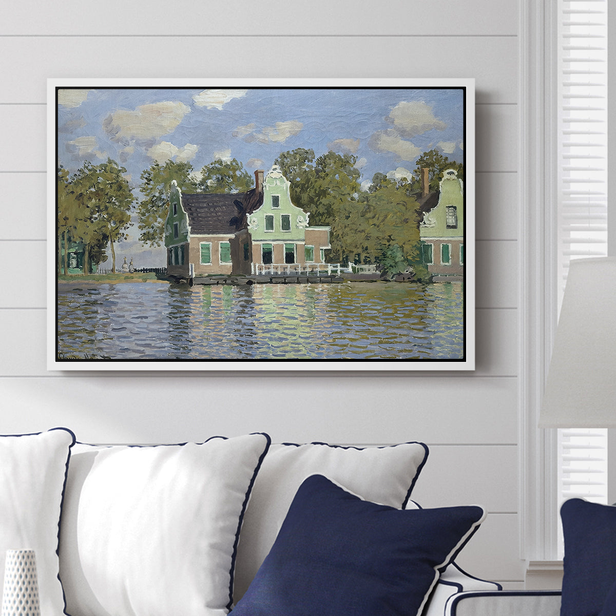 Houses on the Zaan River at Zaandam, 1871 by Claude Monet displayed above a sofa in a living room in a white floater frame, featuring an impressionist riverside village with colorful buildings.