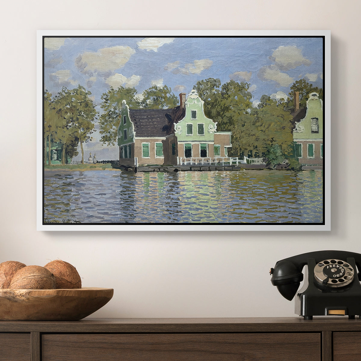Houses on the Zaan River at Zaandam, 1871 by Claude Monet in a white floater framed canvas displayed above a console table in a hallway, featuring a waterfront architecture with still reflections.