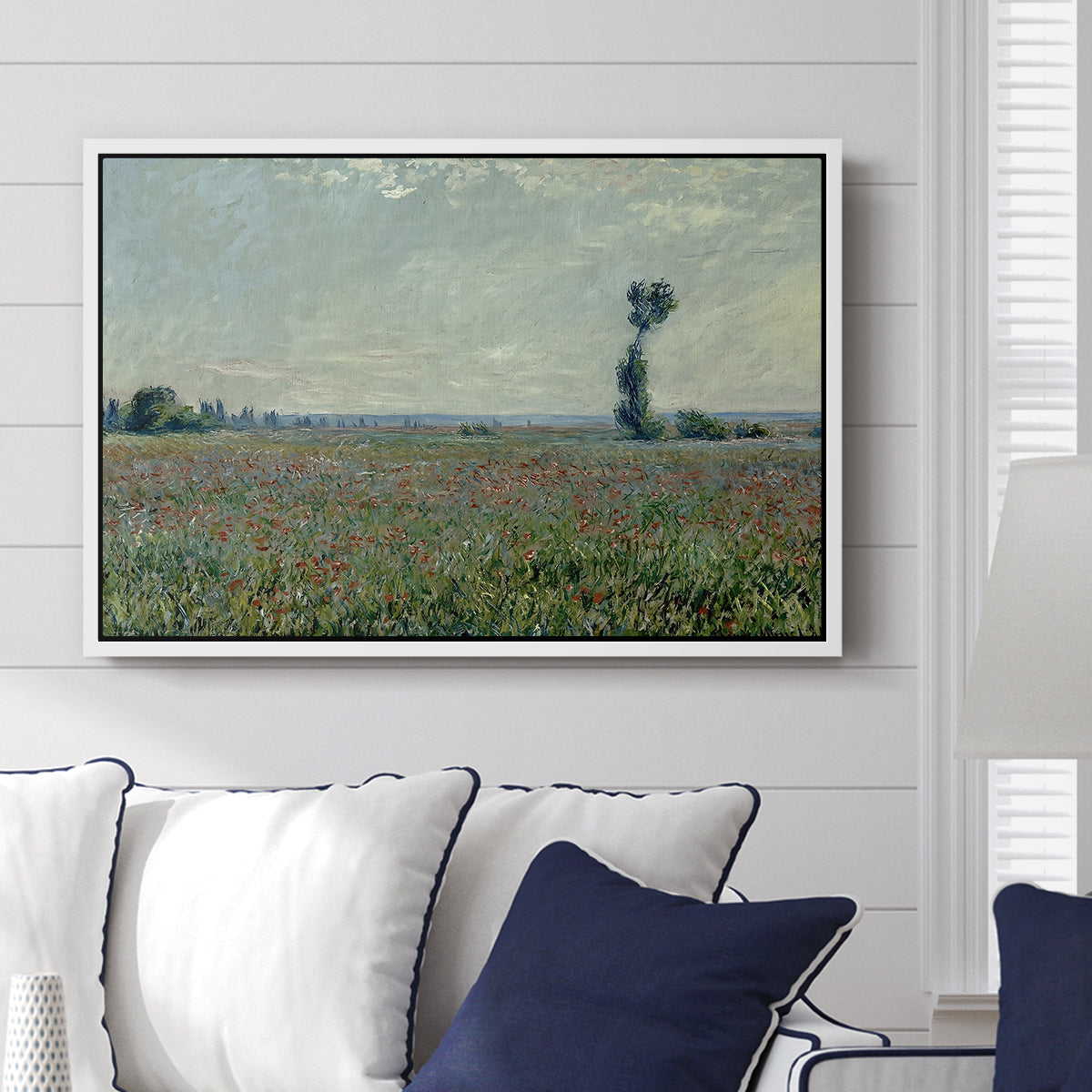 Poppy Field, 1881 by Claude Monet displayed above a sofa in a living room in a white floater frame, featuring an impressionist landscape filled with blooming flowers and greenery.