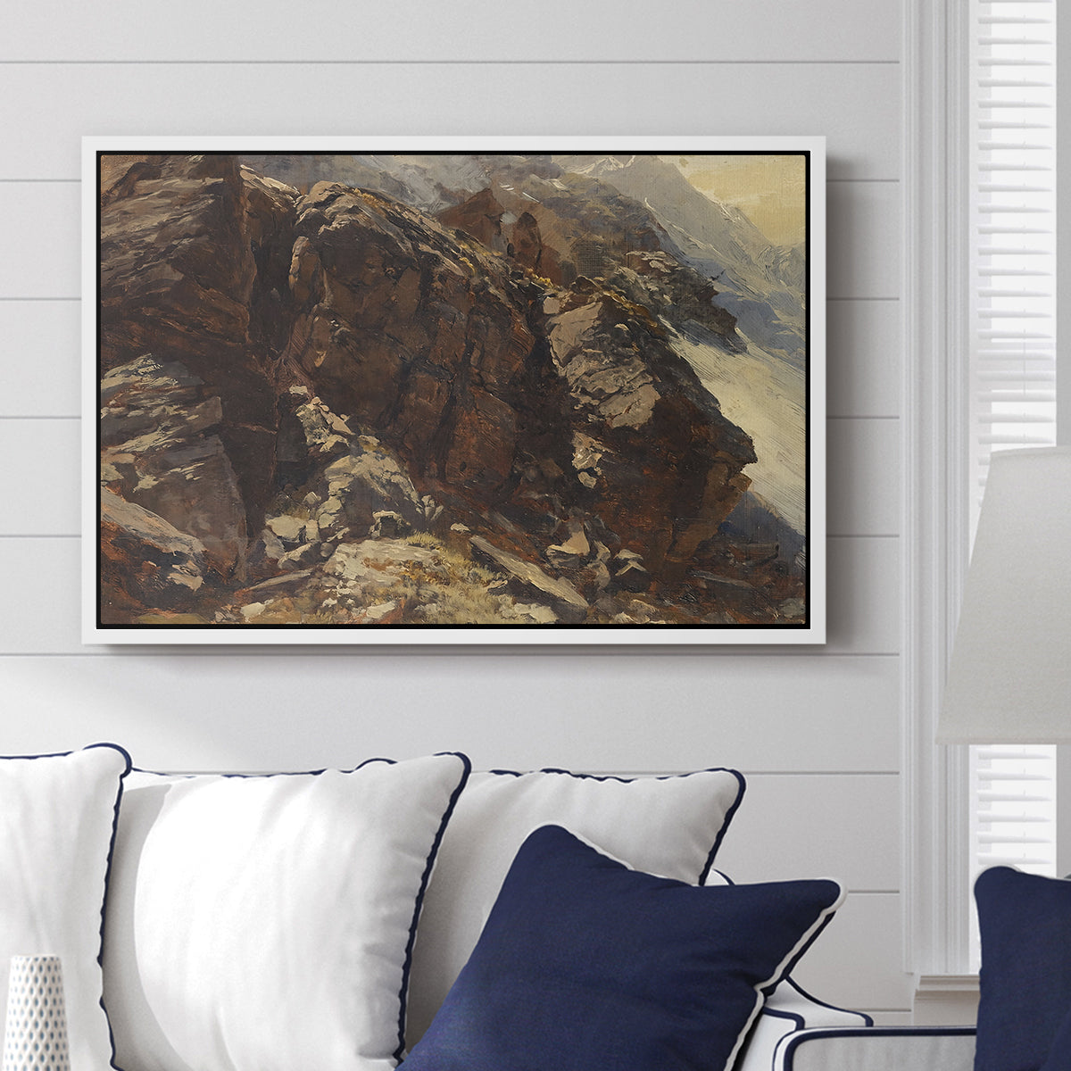 High Mountain Study, c. 1870 by Edward Theodore Compton displayed above a sofa in a living room in a white floater frame, featuring a detailed study of rugged mountain landscape with sharp contours.