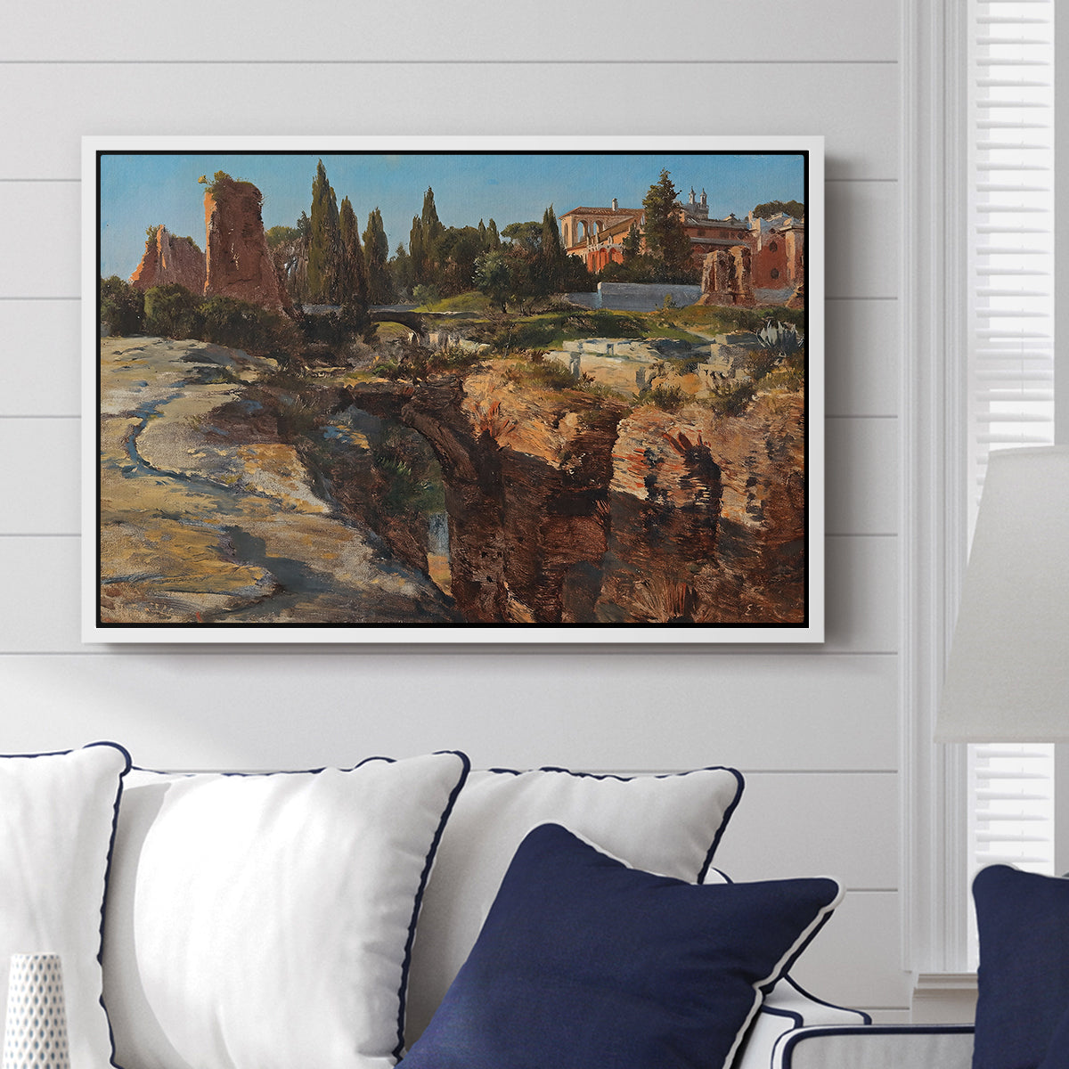 Palatine in Rome, c. 1921 by Edward Theodore Compton displayed above a sofa in a living room in a white floater frame, featuring an architectural scene of ancient structures in sunlit environment.