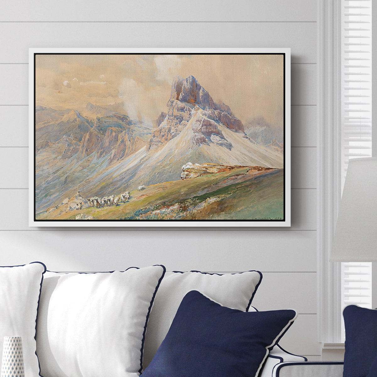 From the Dolomites, 1904 by Edward Theodore Compton displayed above a sofa in a living room in a white floater frame, featuring an alpine scene with jagged rock formations and distant mountains.
