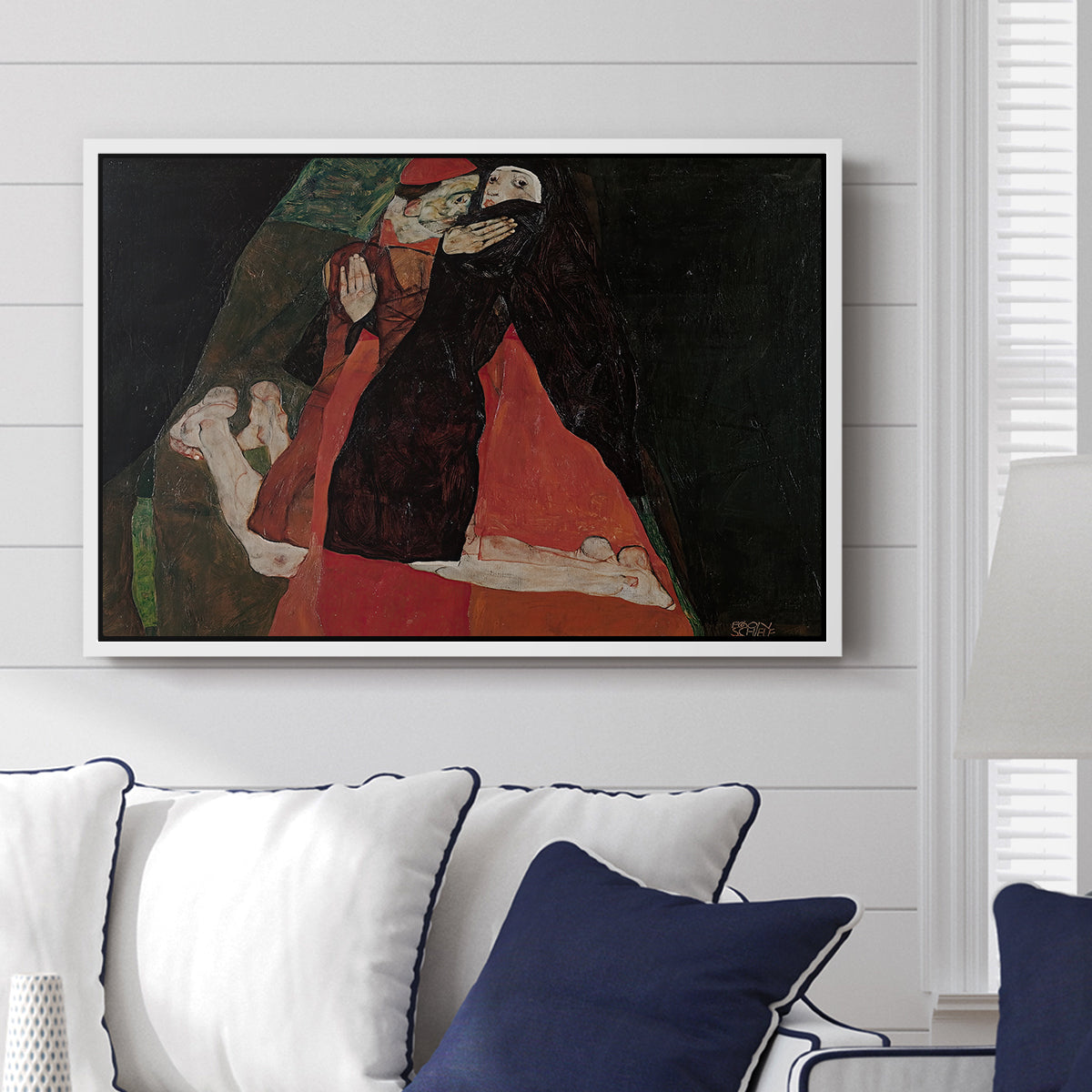 Cardinal and Nun (Caress), 1912 by Egon Schiele displayed above a sofa in a living room in a white floater frame, featuring a cardinal and nun depicted in close emotional interaction.