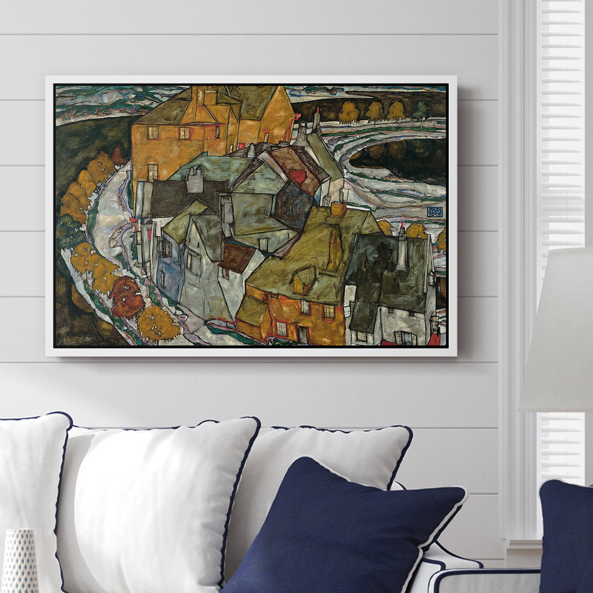 Crescent of Houses II (Island Town), 1915 by Egon Schiele displayed above a sofa in a living room in a white floater frame, featuring a stylized townscape with clustered buildings and bold outlines.