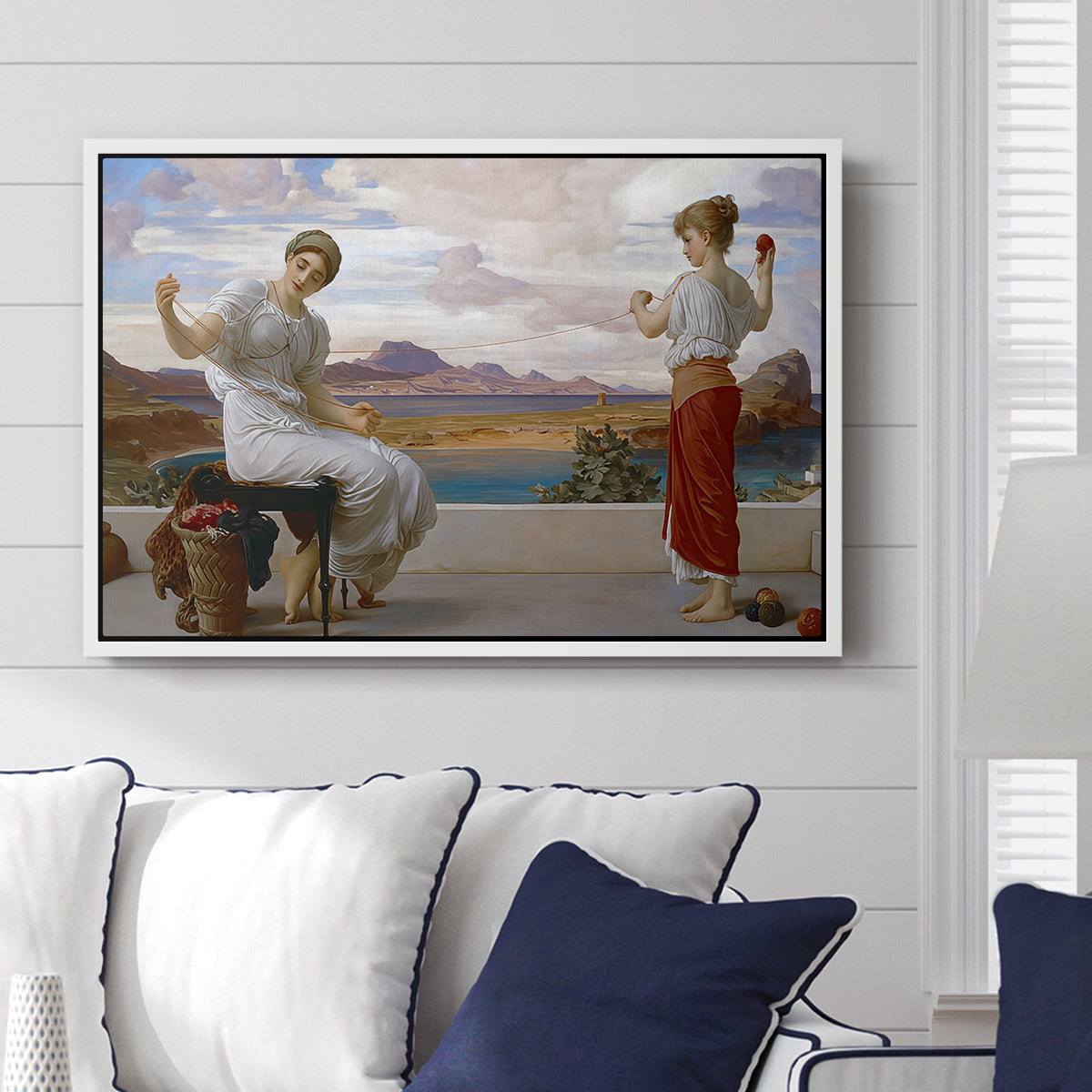Winding the Skein, c. 1878 by Frederic Leighton displayed above a sofa in a living room in a white floater frame, featuring two women engaged in textile work with draped garments.