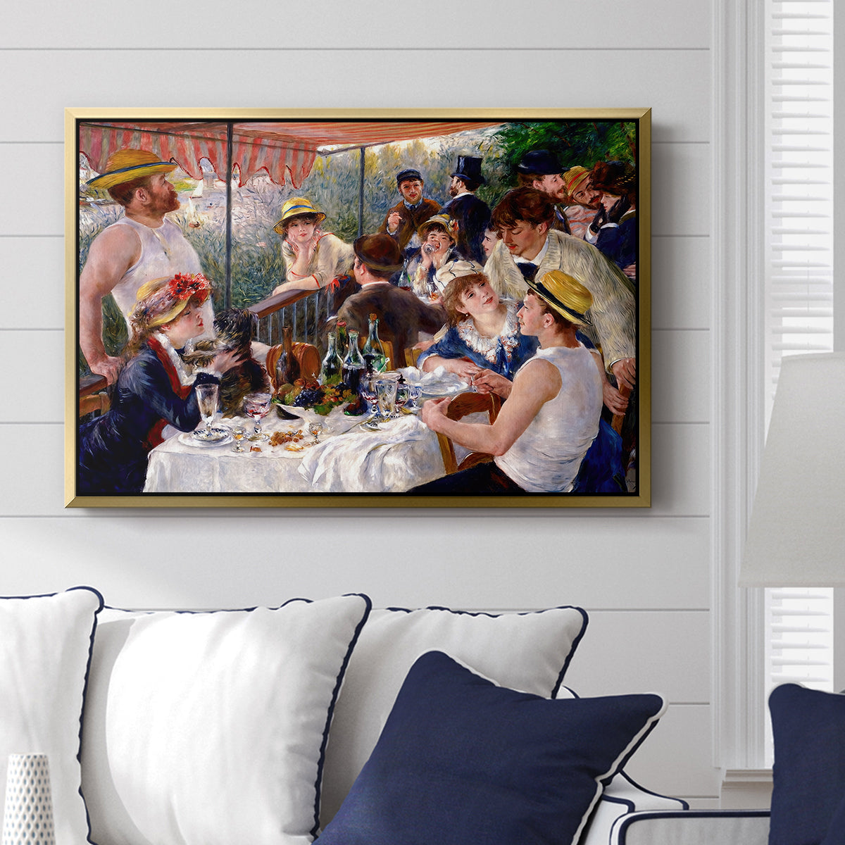 Luncheon of the Boating Party (Le Déjeuner des canotiers), 1880-1881 by Pierre-Auguste Renoir displayed above a sofa in a living room in a gold floater frame, featuring a lively gathering of men and women eating and socializing at outdoor table.