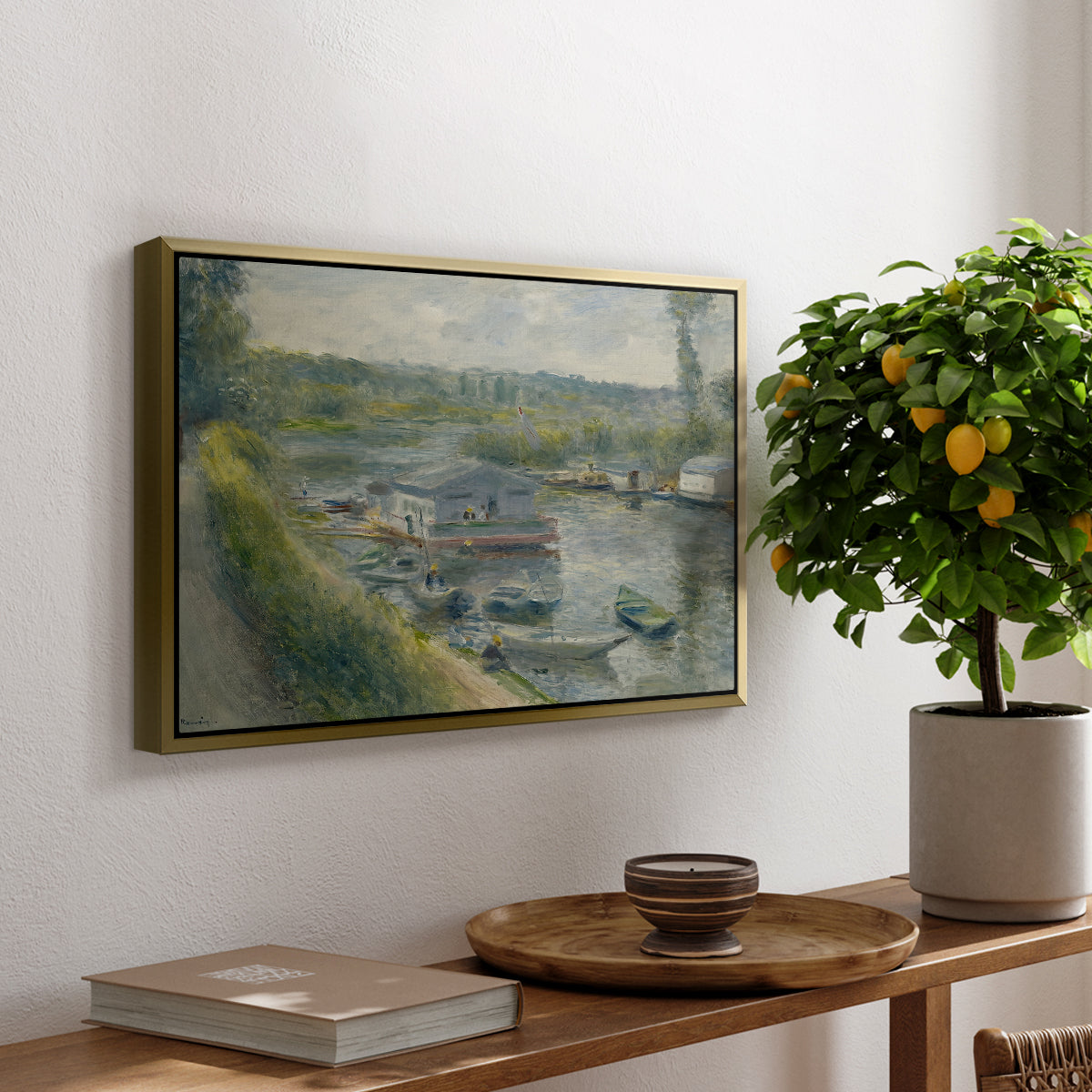 Wash-House Boat at Bas-Meudon, c. 1874 by Pierre-Auguste Renoir, presented in a gold floater framed canvas featuring a floating wash-house boat along a riverbank with figures working nearby, displayed above a hallway console table.