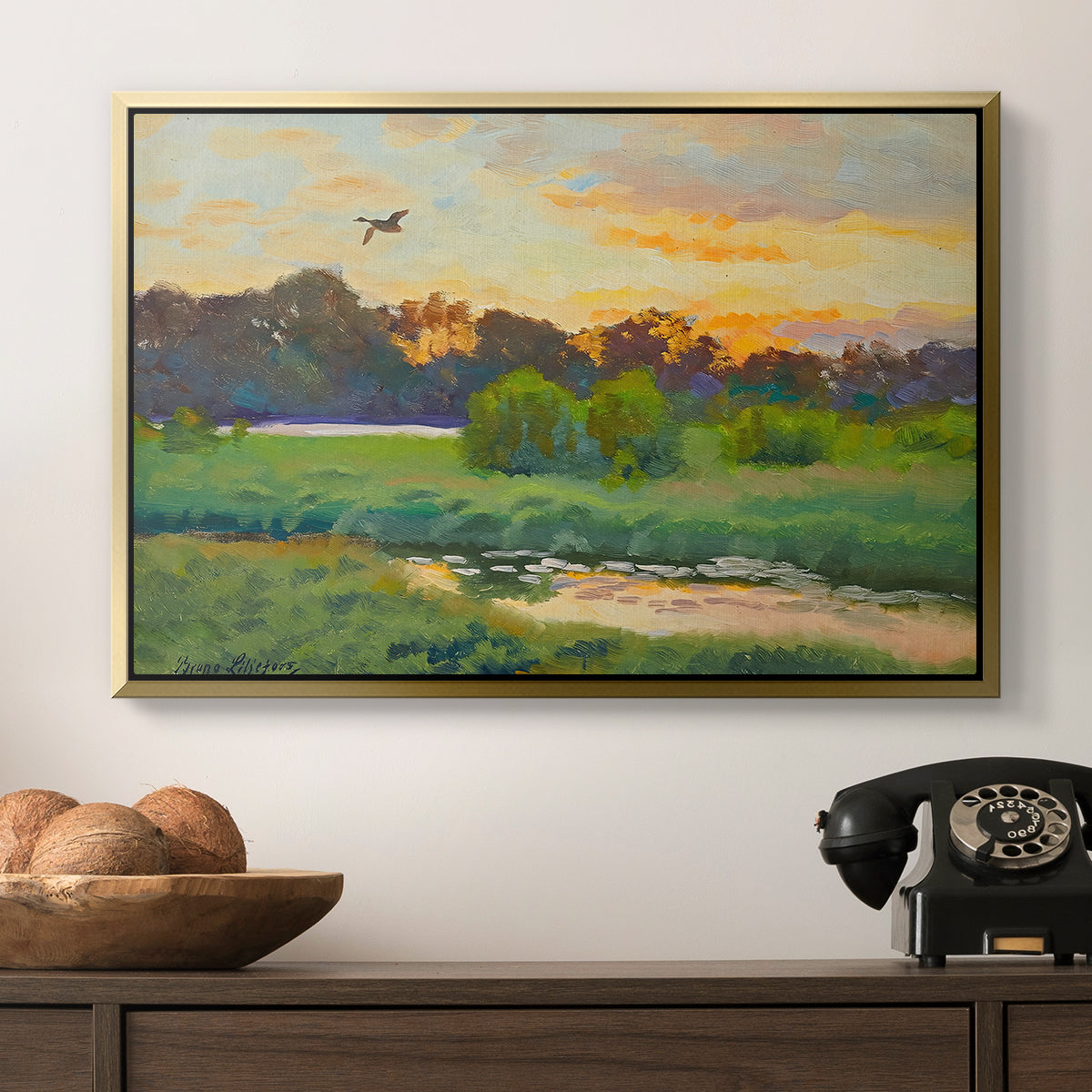 Flying Duck at Sunset, 1924 by Bruno Liljefors in a gold floater framed canvas displayed above a console table in a hallway, featuring a lone duck flying over a marsh at golden hour.