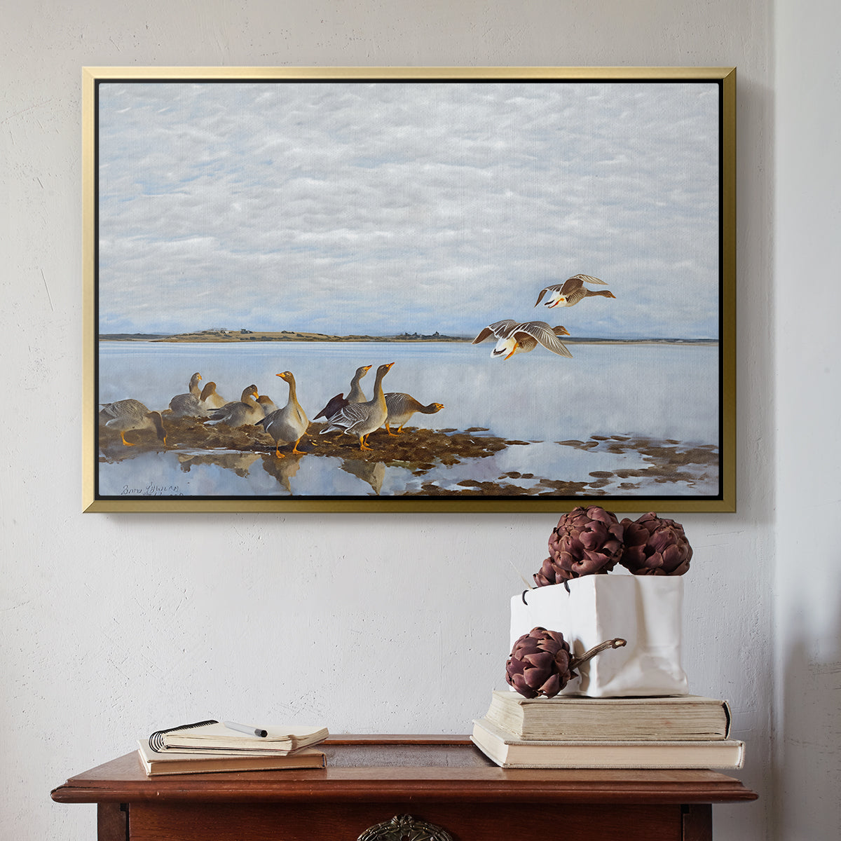 Gold floater framed canvas featuring Greylag Geese (Grågäss), 1922 by Bruno Liljefors above an entryway table in a minimalist foyer.