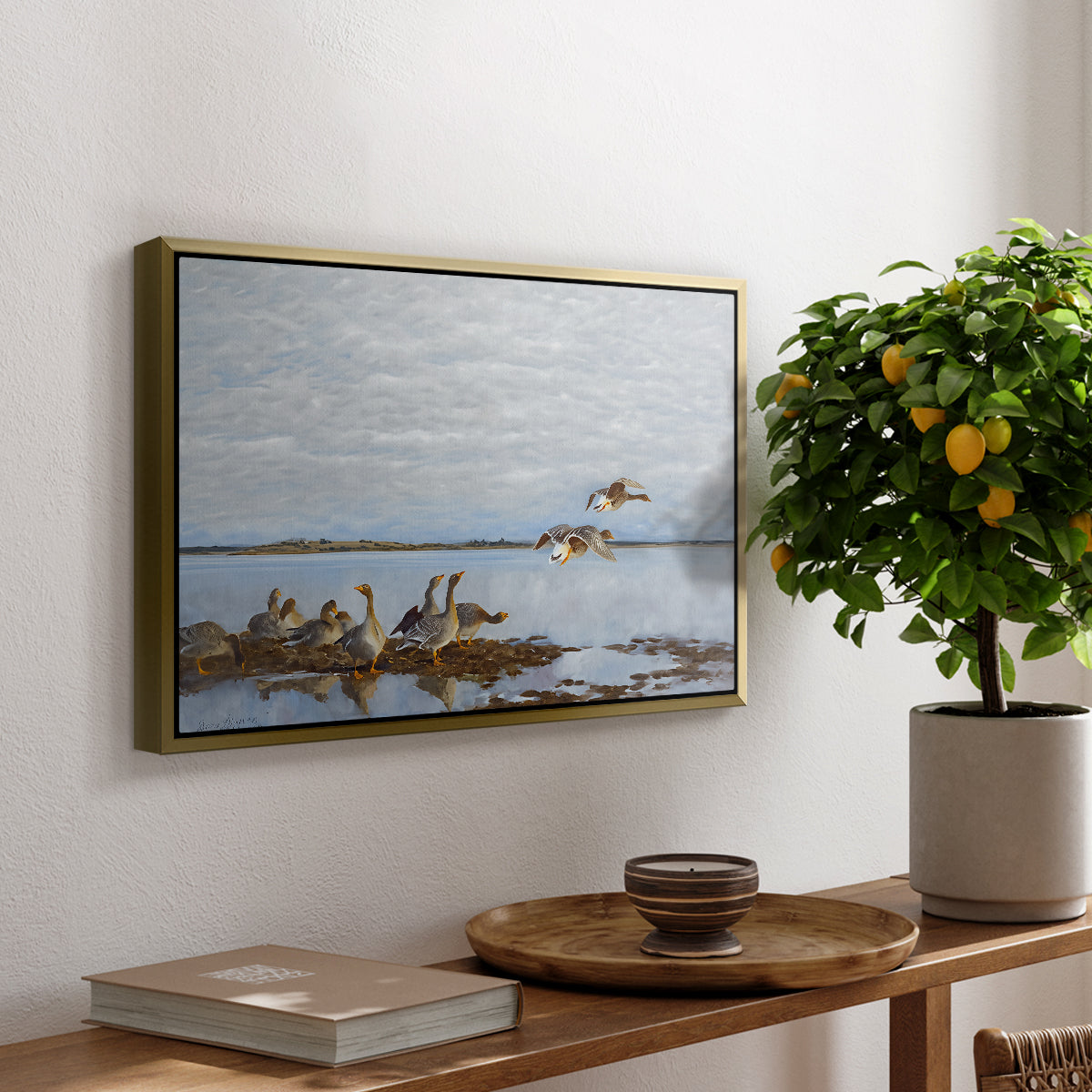 Greylag Geese (Grågäss), 1922 by Bruno Liljefors, presented in a gold floater framed canvas featuring a group of geese gathered near water in a natural wetland landscape, displayed above a hallway console table.