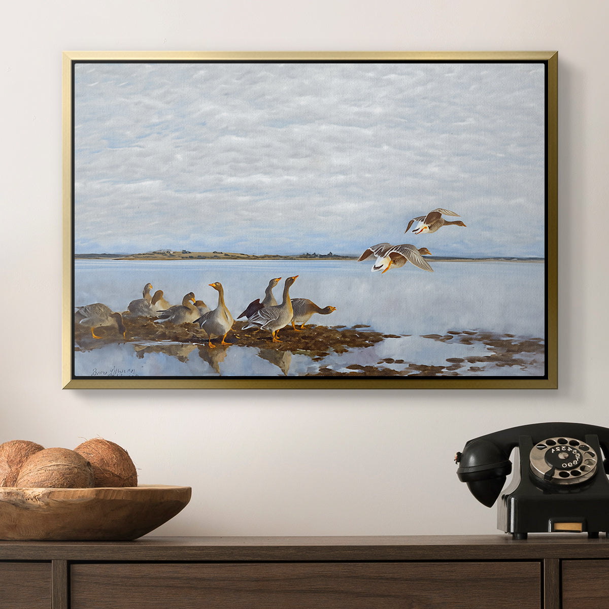 Greylag Geese (Grågäss), 1922 by Bruno Liljefors in a gold floater framed canvas displayed above a console table in a hallway, featuring a flock of geese positioned along marshy terrain.