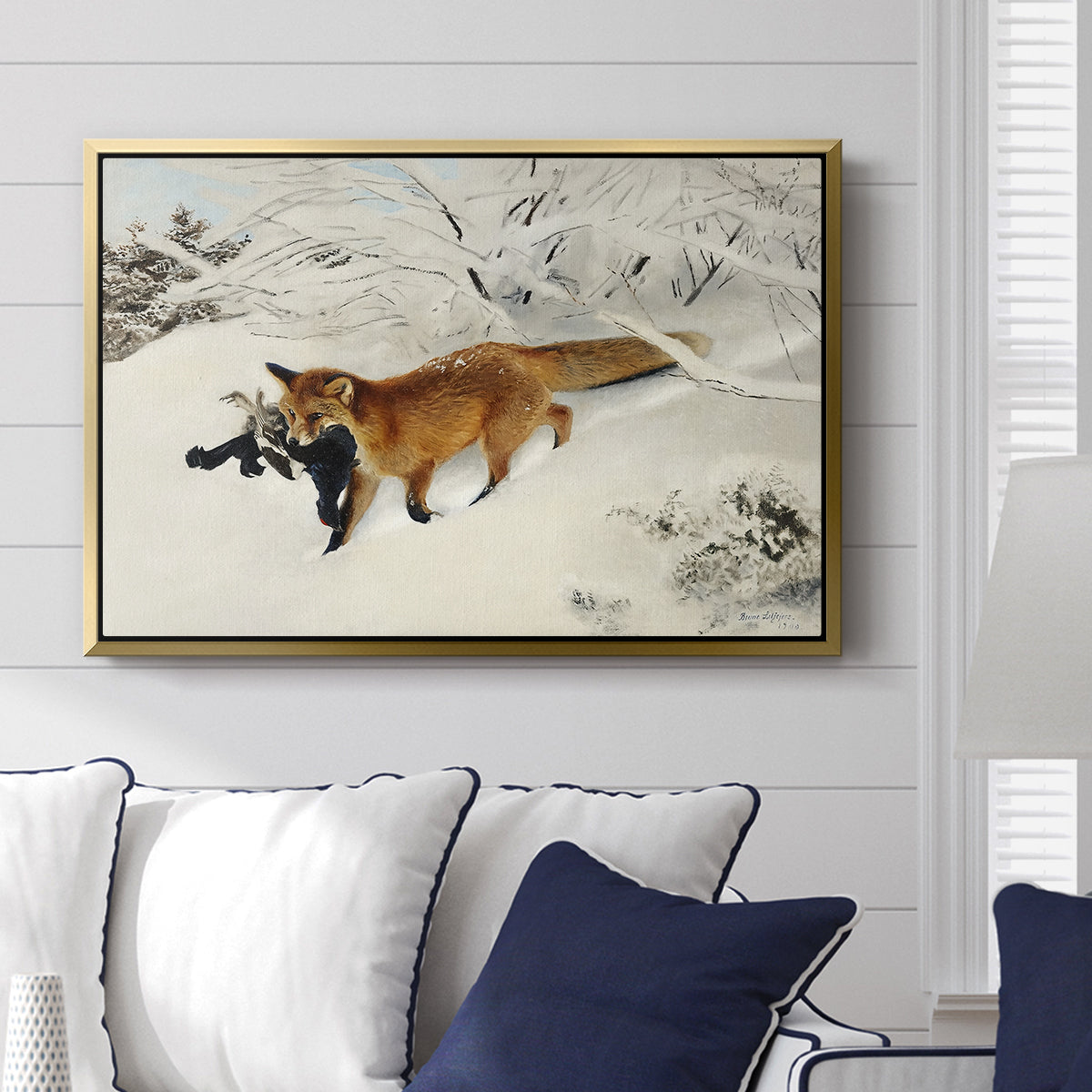 Fox in Snow Landscape, 1900 by Bruno Liljefors displayed above a sofa in a living room in a gold floater frame, featuring a wildlife scene of fox moving swiftly through winter terrain.