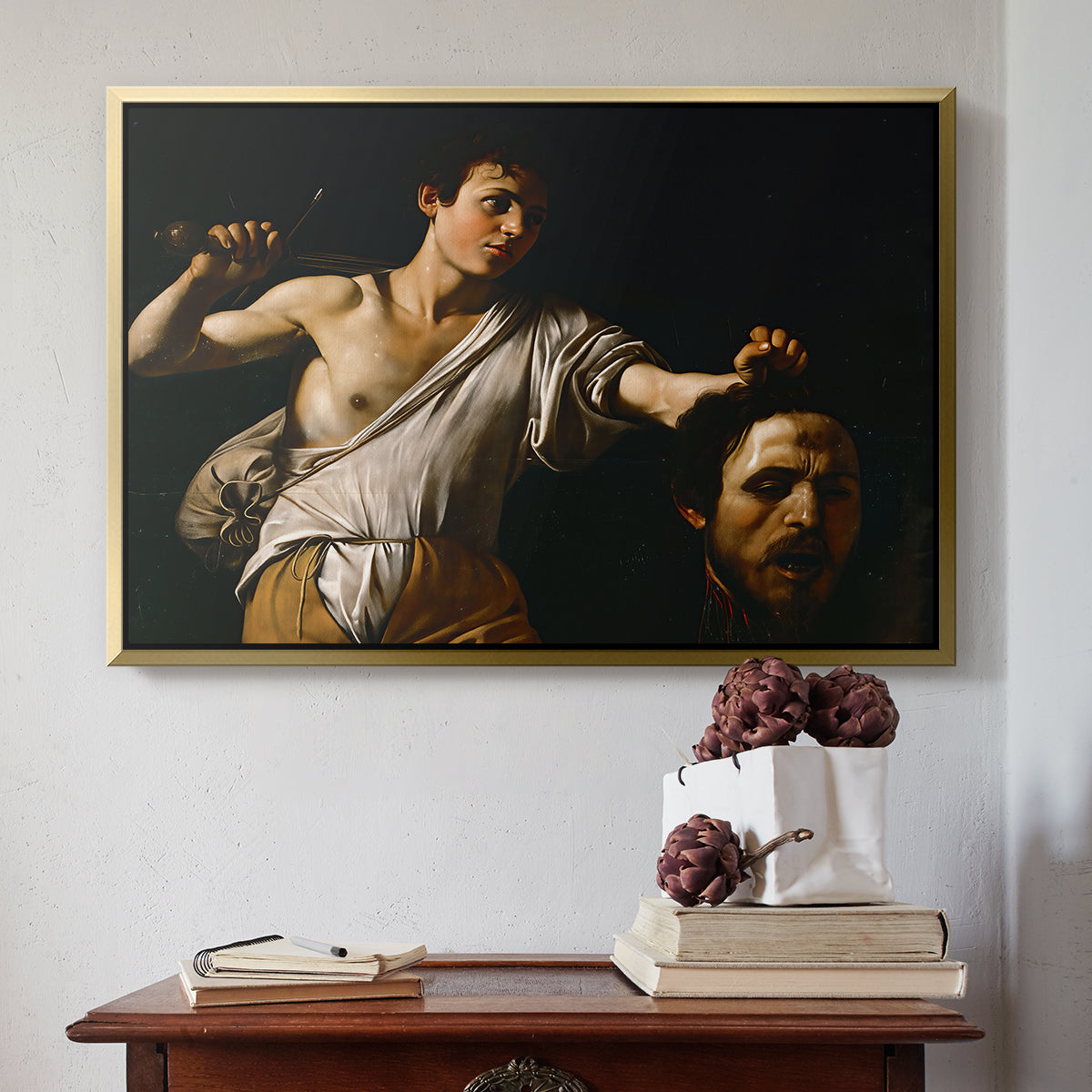 Gold floater framed canvas featuring David with the Head of Goliath (Vienna Version), c. 1607 by Caravaggio above an entryway table in a minimalist foyer.