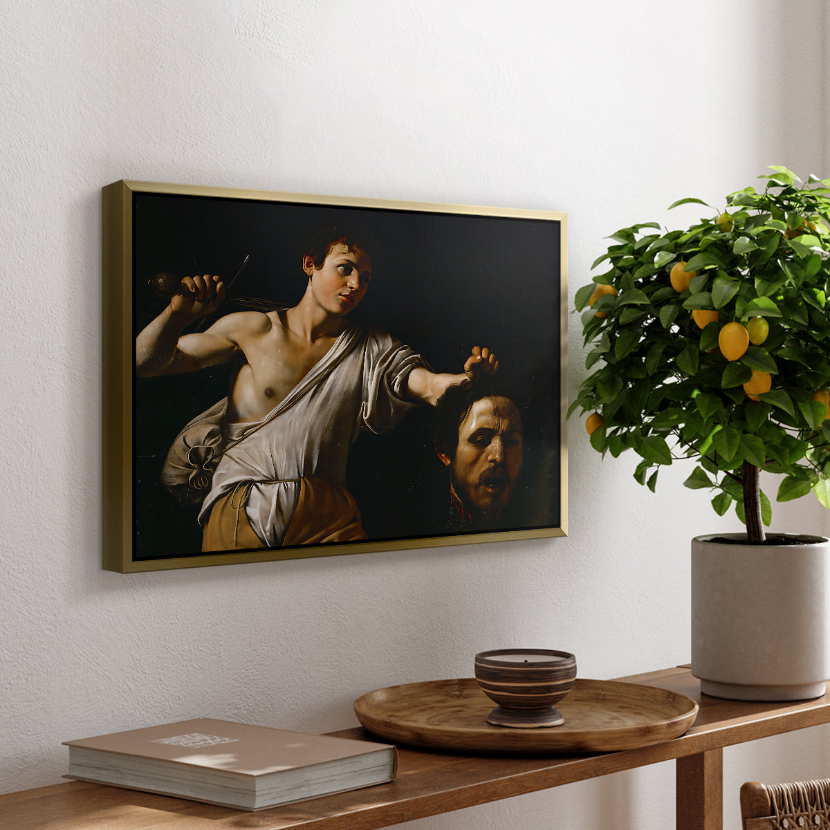 David with the Head of Goliath (Vienna Version), c. 1607 by Caravaggio, presented in a gold floater framed canvas featuring a young David holding the severed head of Goliath against a dark background, displayed above a hallway console table.