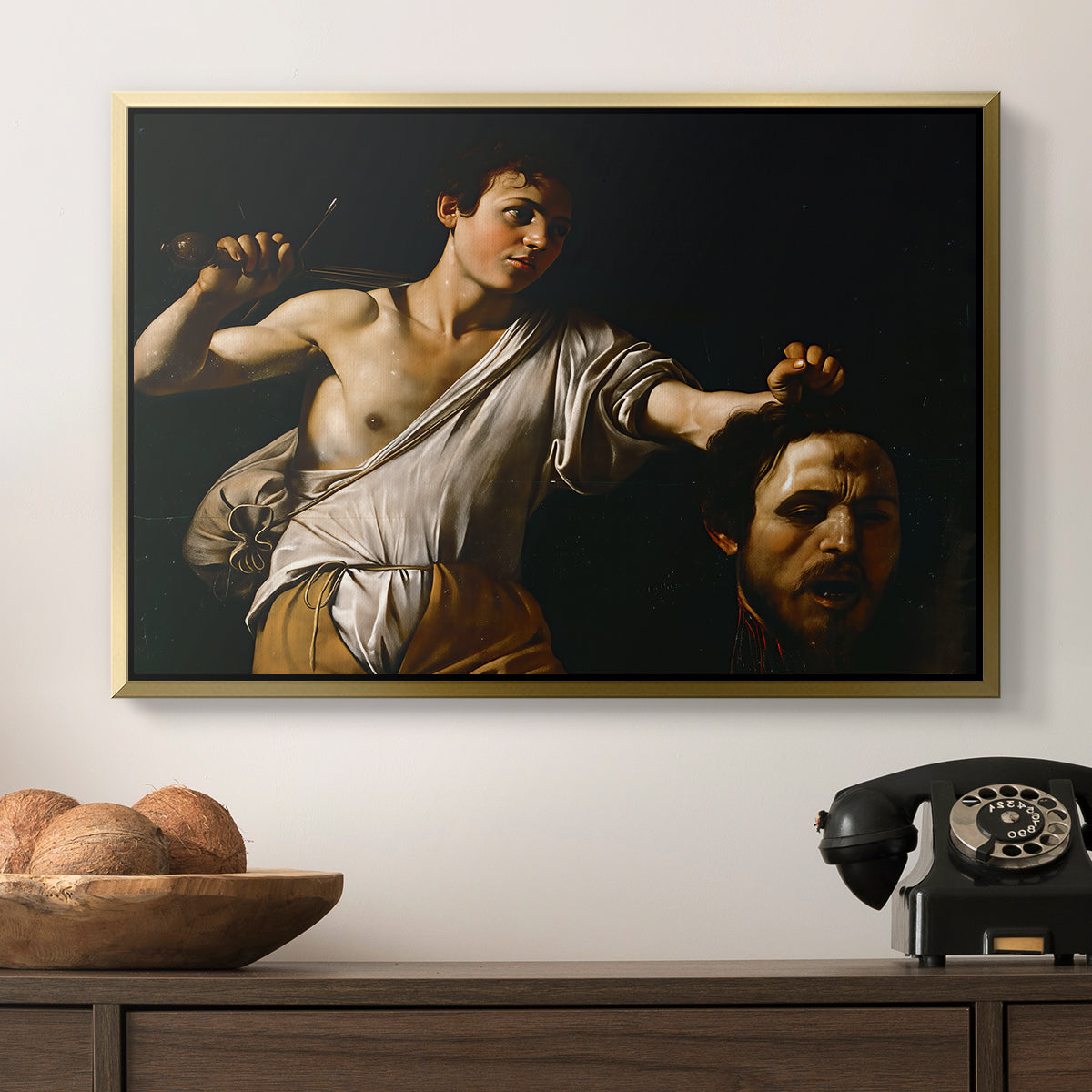 David with the Head of Goliath (Vienna Version), c. 1607 by Caravaggio in a gold floater framed canvas displayed above a console table in a hallway, featuring an intense religious scene with figure emerging from darkness holding trophy.