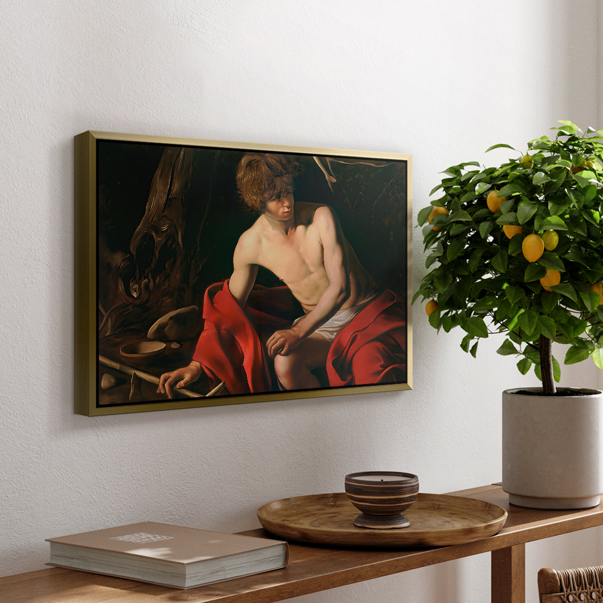 Saint John the Baptist in the Wilderness, c. 1603-1604 by Caravaggio, presented in a gold floater framed canvas featuring a young Saint John seated in wilderness with staff and red drapery, displayed above a hallway console table.