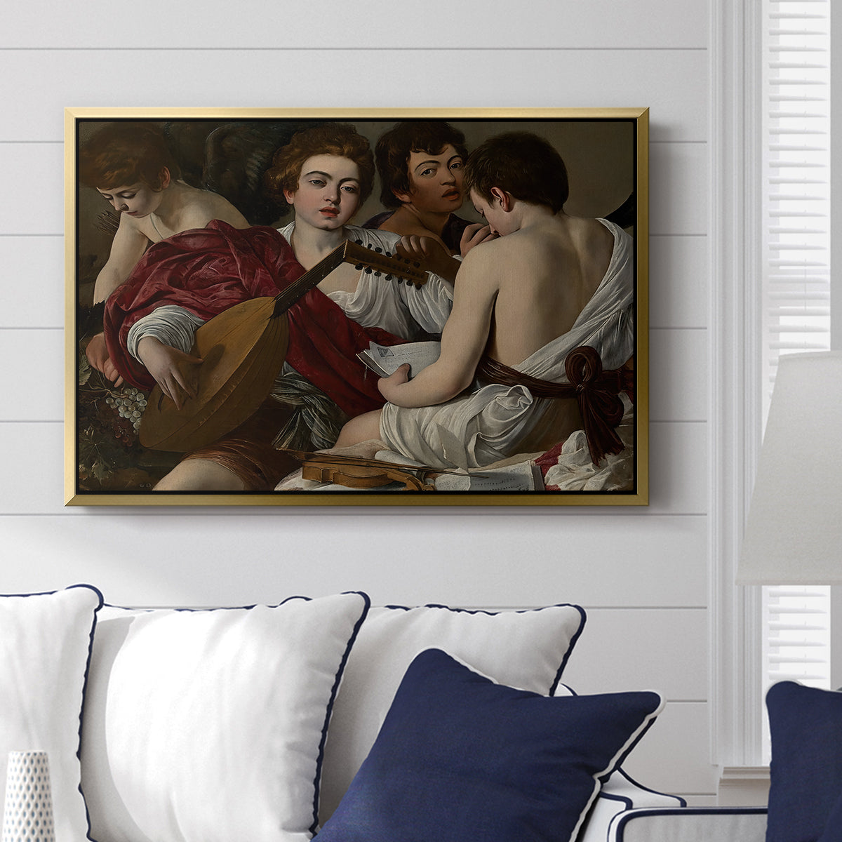 The Musicians, c. 1595 by Caravaggio displayed above a sofa in a living room in a gold floater frame, featuring an ensemble of musicians holding lute and singing in close arrangement.