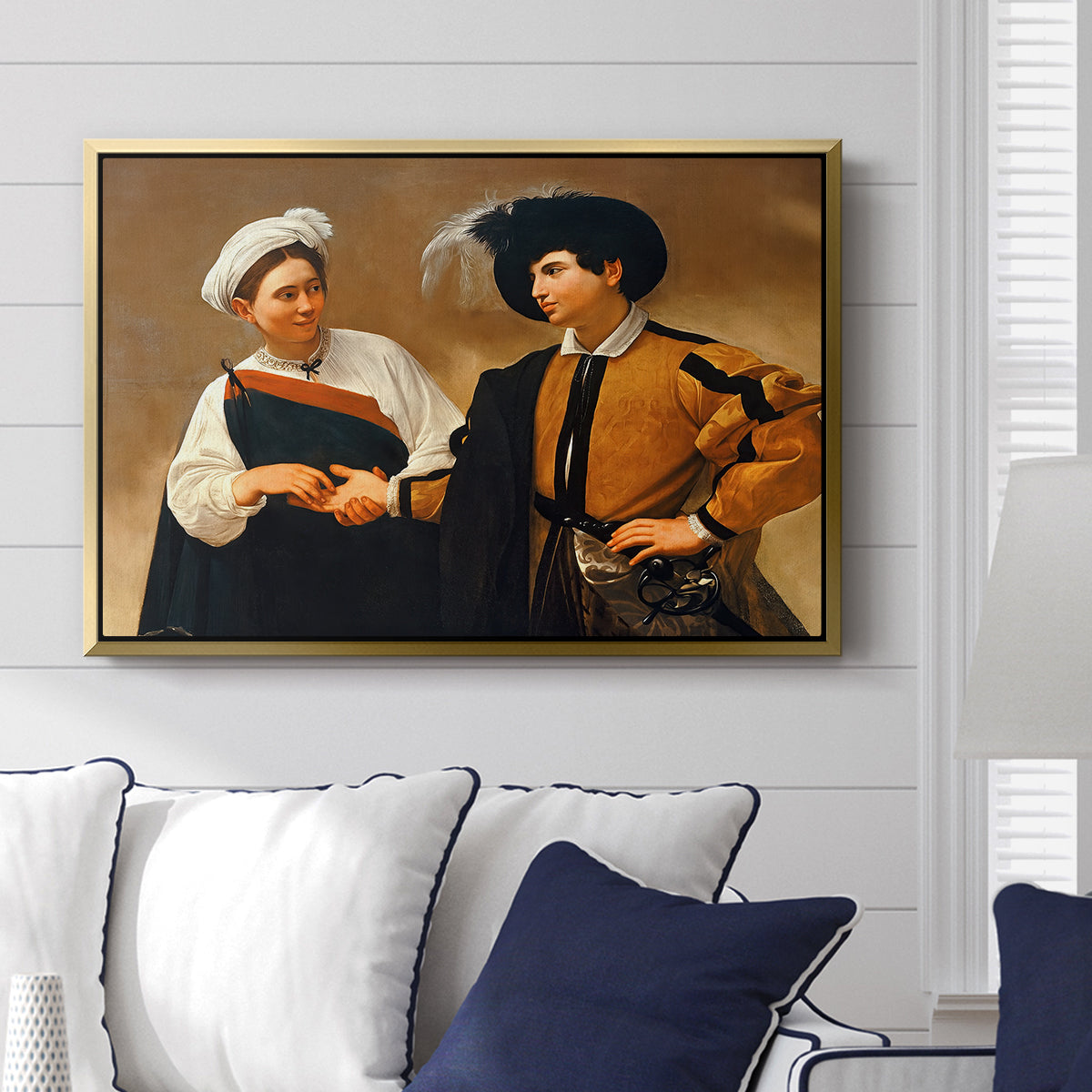 The Fortune Teller (Capitoline Version), c. 1599 by Caravaggio displayed above a sofa in a living room in a gold floater frame, featuring a fortune teller tricking young man during palm reading.