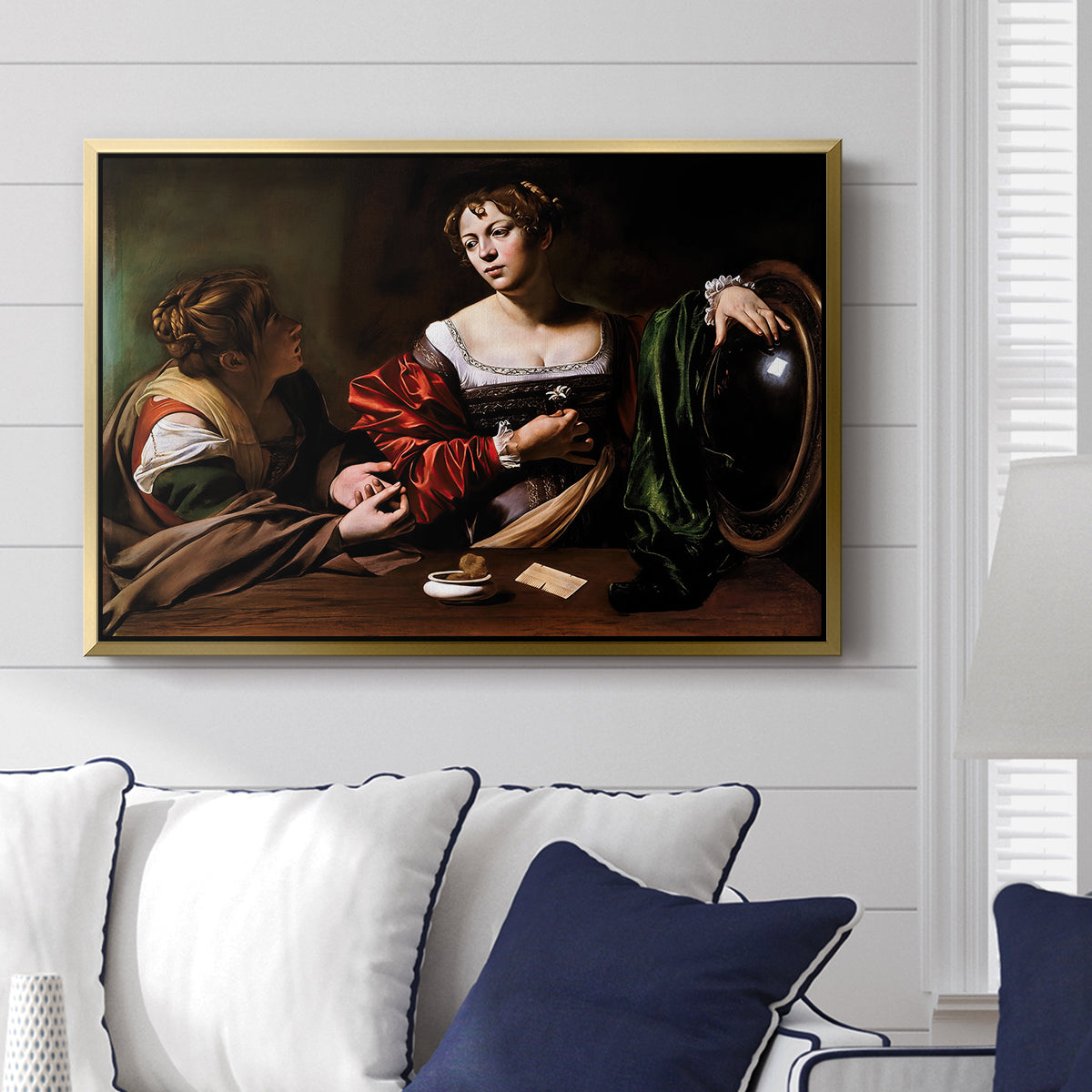 Martha and Mary Magdalene, c. 1598 by Caravaggio displayed above a sofa in a living room in a gold floater frame, featuring a biblical scene of Martha speaking to Mary Magdalene indoors.