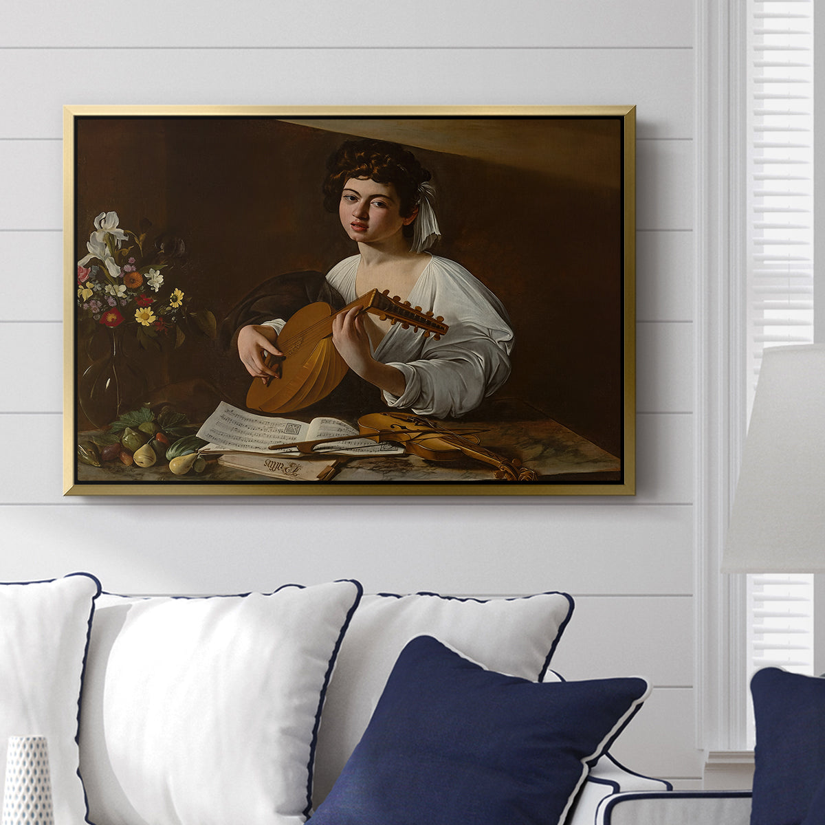 The Lute Player (Hermitage Version), c. 1596 by Caravaggio displayed above a sofa in a living room in a gold floater frame, featuring a portrait of lute player surrounded by still life arrangement.
