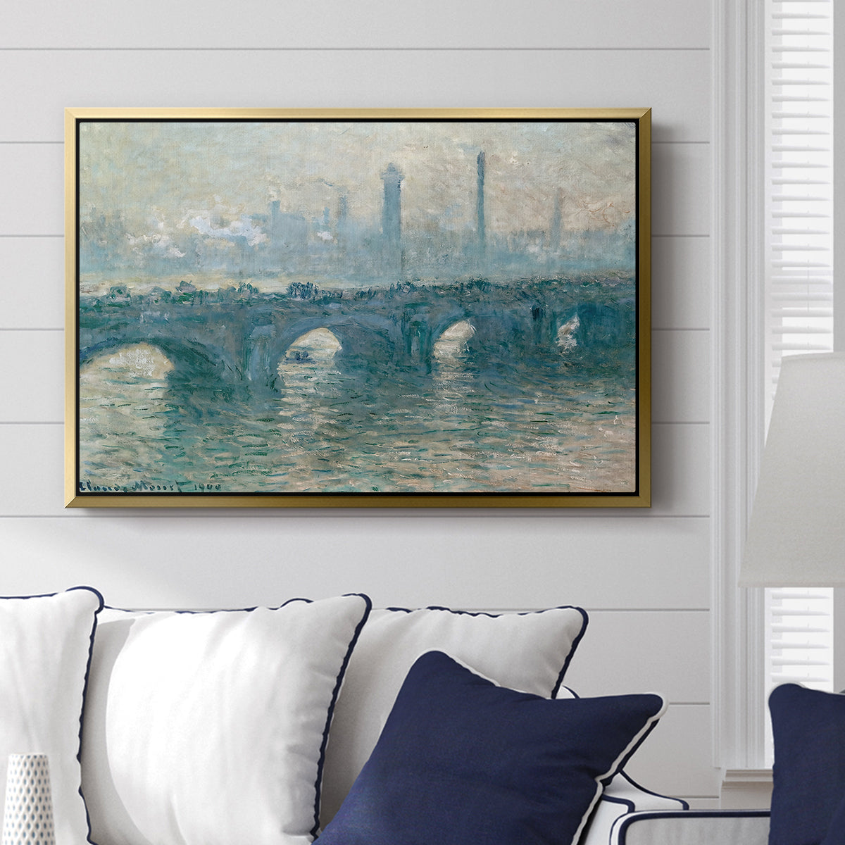 Waterloo Bridge, Gray Weather, 1900 by Claude Monet displayed above a sofa in a living room in a gold floater frame, featuring an impressionist cityscape with bridge fading into fog over water.