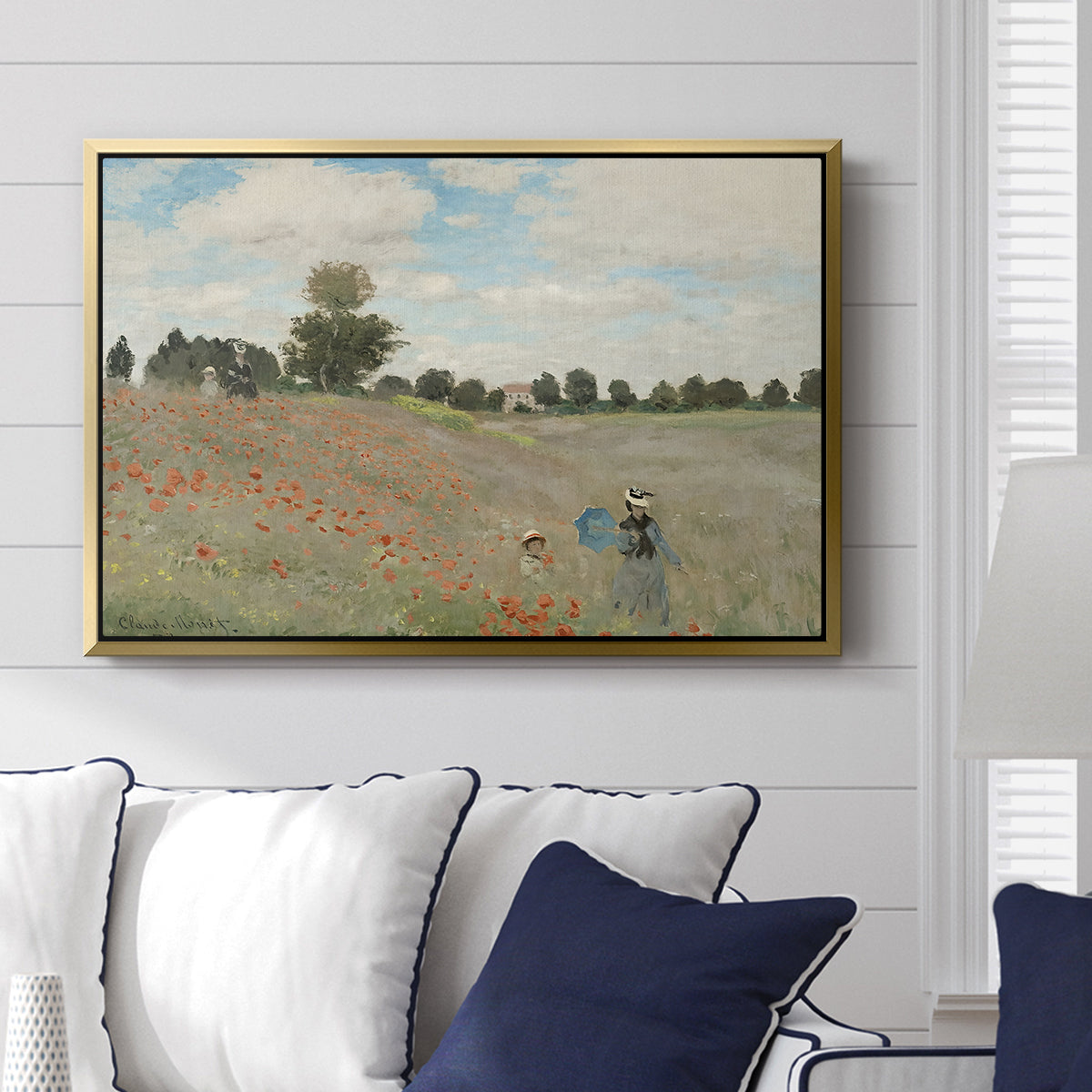 The Poppy Field near Argenteuil, 1873 by Claude Monet displayed above a sofa in a living room in a gold floater frame, featuring an impressionist countryside scene with flowers and strolling figures.