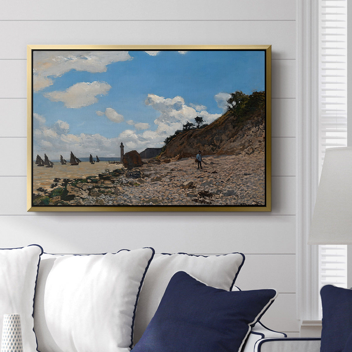 The Beach at Honfleur, 1864 by Claude Monet displayed above a sofa in a living room in a gold floater frame, featuring an impressionist seaside with people and sailboats under bright sky.