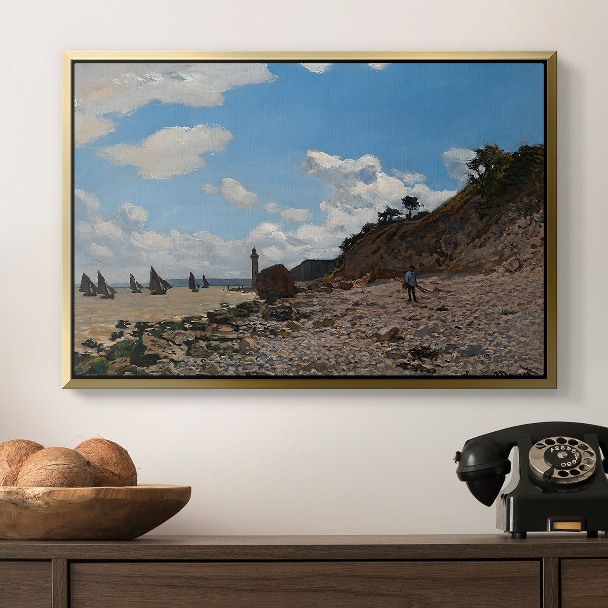 The Beach at Honfleur, 1864 by Claude Monet in a gold floater framed canvas displayed above a console table in a hallway, featuring a coastal landscape with boats and people along shore.