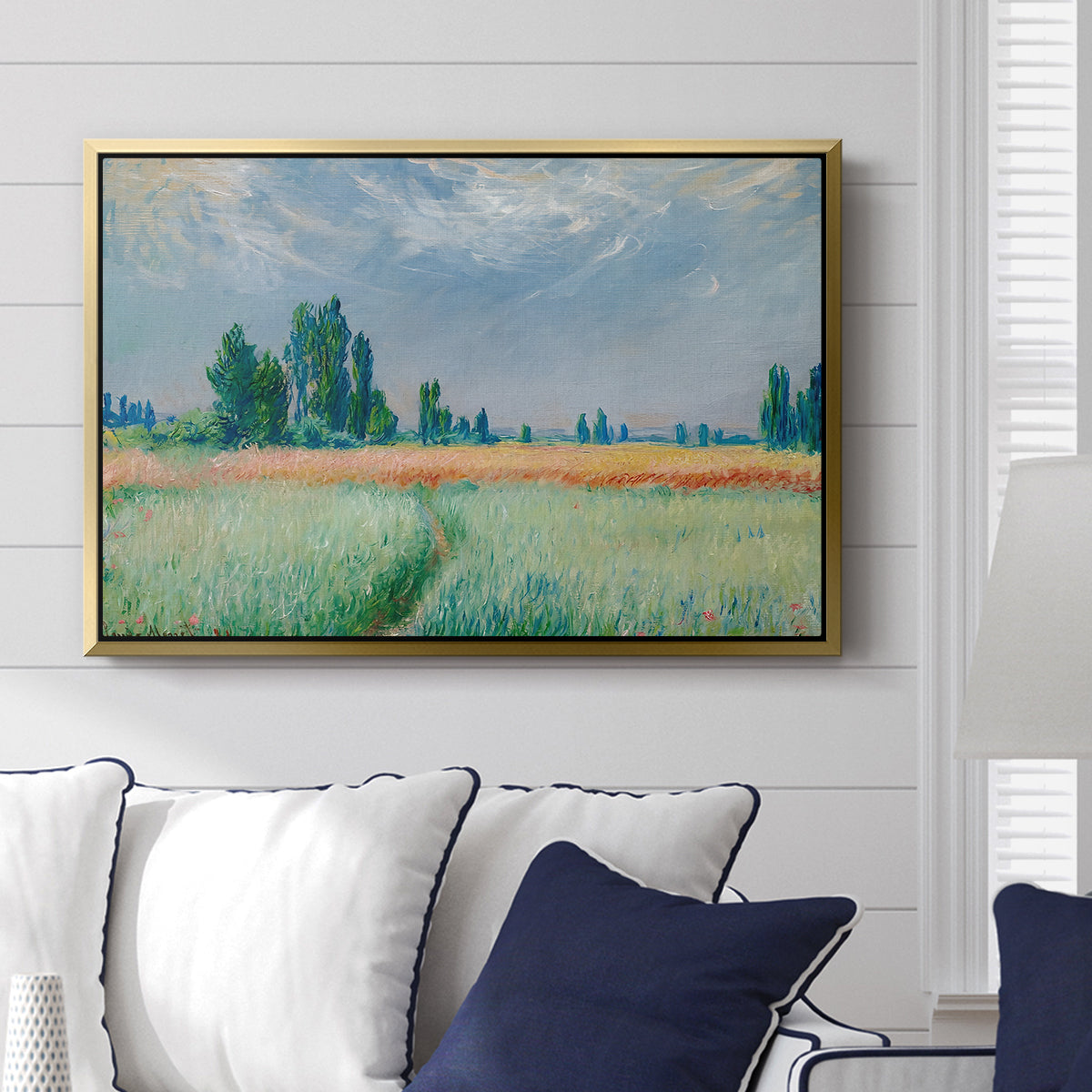The Wheat Field (Champ de Blé), 1881 by Claude Monet displayed above a sofa in a living room in a gold floater frame, featuring an impressionist depiction of ripened grain field in countryside.