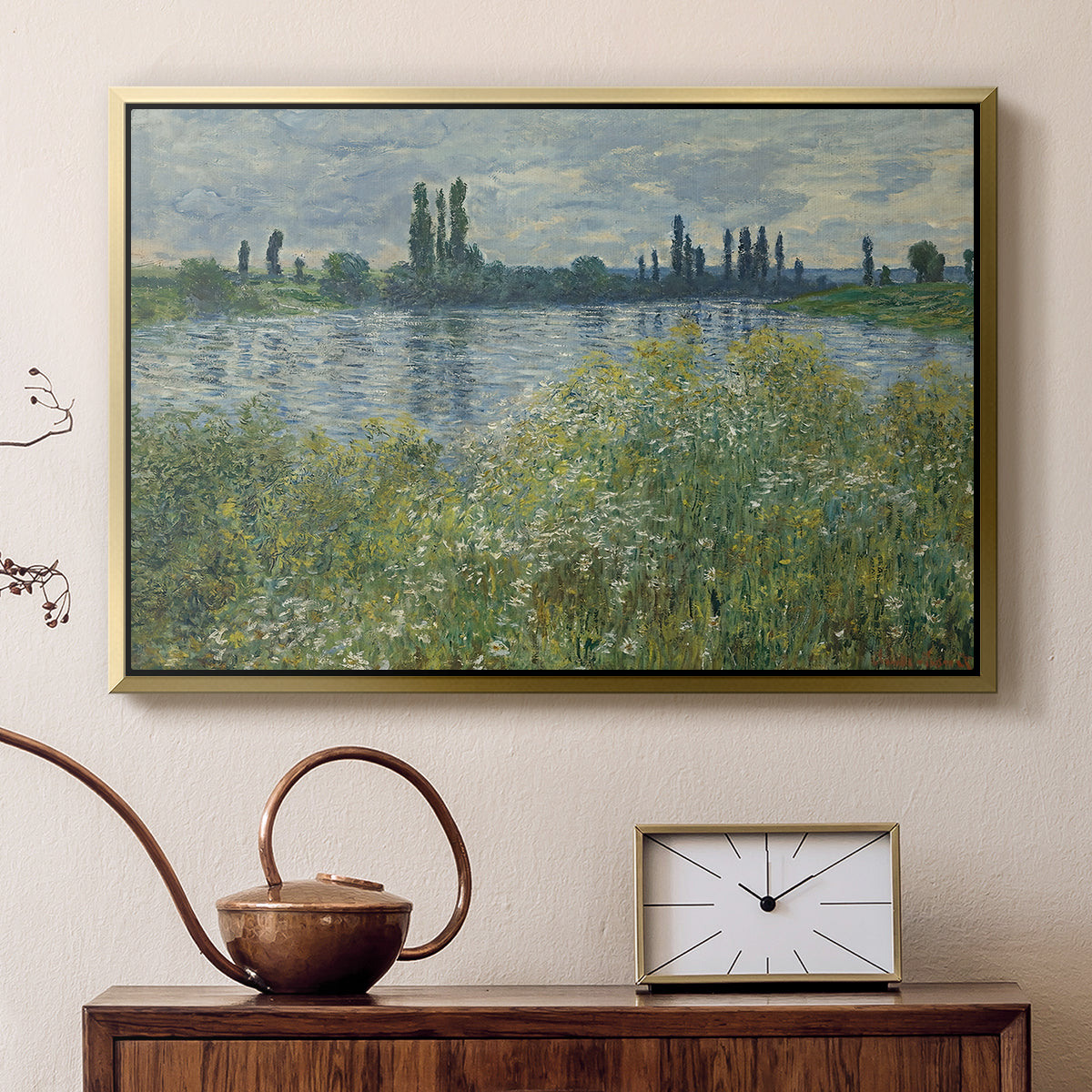 Gold floater framed canvas featuring a tranquil riverside scene with houses and vegetation, displayed above a cabinet in a soft-toned living room.