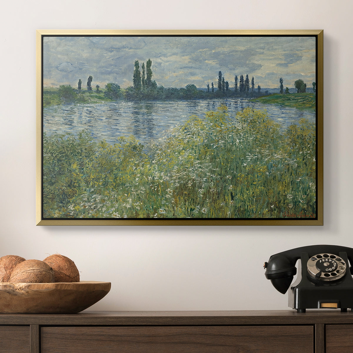 Banks of the Seine, Vétheuil, 1880 by Claude Monet in a gold floater framed canvas displayed above a console table in a hallway, featuring a natural landscape with calm water and soft foliage.