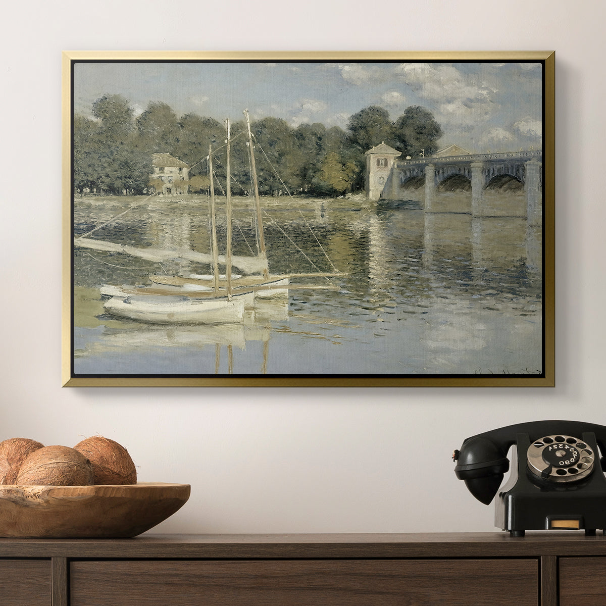 The Bridge at Argenteuil, 1874 by Claude Monet in a gold floater framed canvas displayed above a console table in a hallway, featuring a riverside view with architecture and nautical activity.