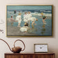 Gold floater framed canvas featuring an impressionist coastal view of families enjoying seaside water, displayed above a cabinet in a soft-toned living room.
