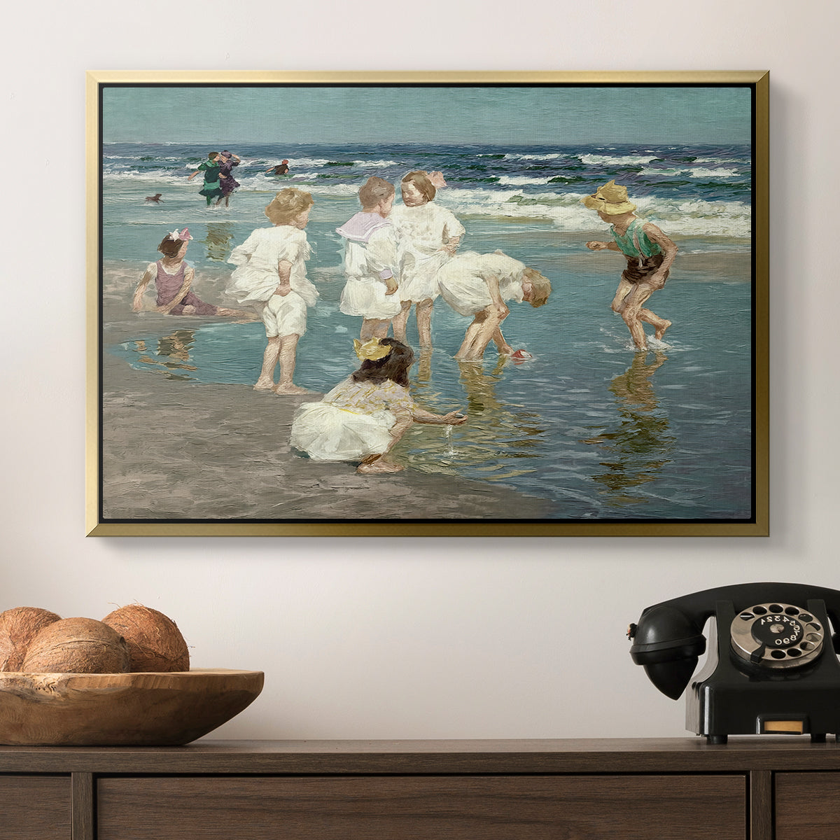 A Holiday, c. 1915 by Edward Henry Potthast in a gold floater framed canvas displayed above a console table in a hallway, featuring a lively shoreline scene with people gathered in surf.