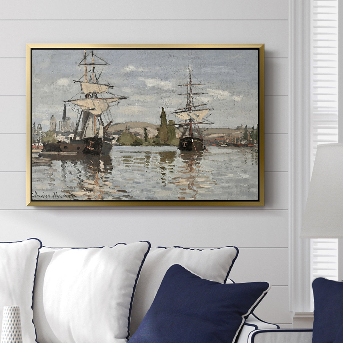 Ships Riding on the Seine at Rouen, 1872 by Claude Monet displayed above a sofa in a living room in a gold floater frame, featuring an impressionist river scene with anchored sailing ships and reflections.