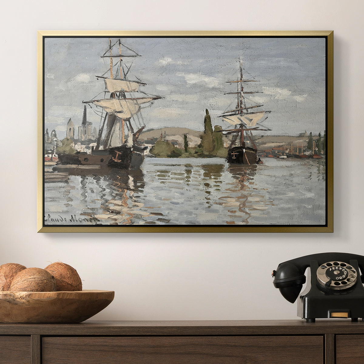Ships Riding on the Seine at Rouen, 1872 by Claude Monet in a gold floater framed canvas displayed above a console table in a hallway, featuring a nautical landscape with vessels resting on calm water.