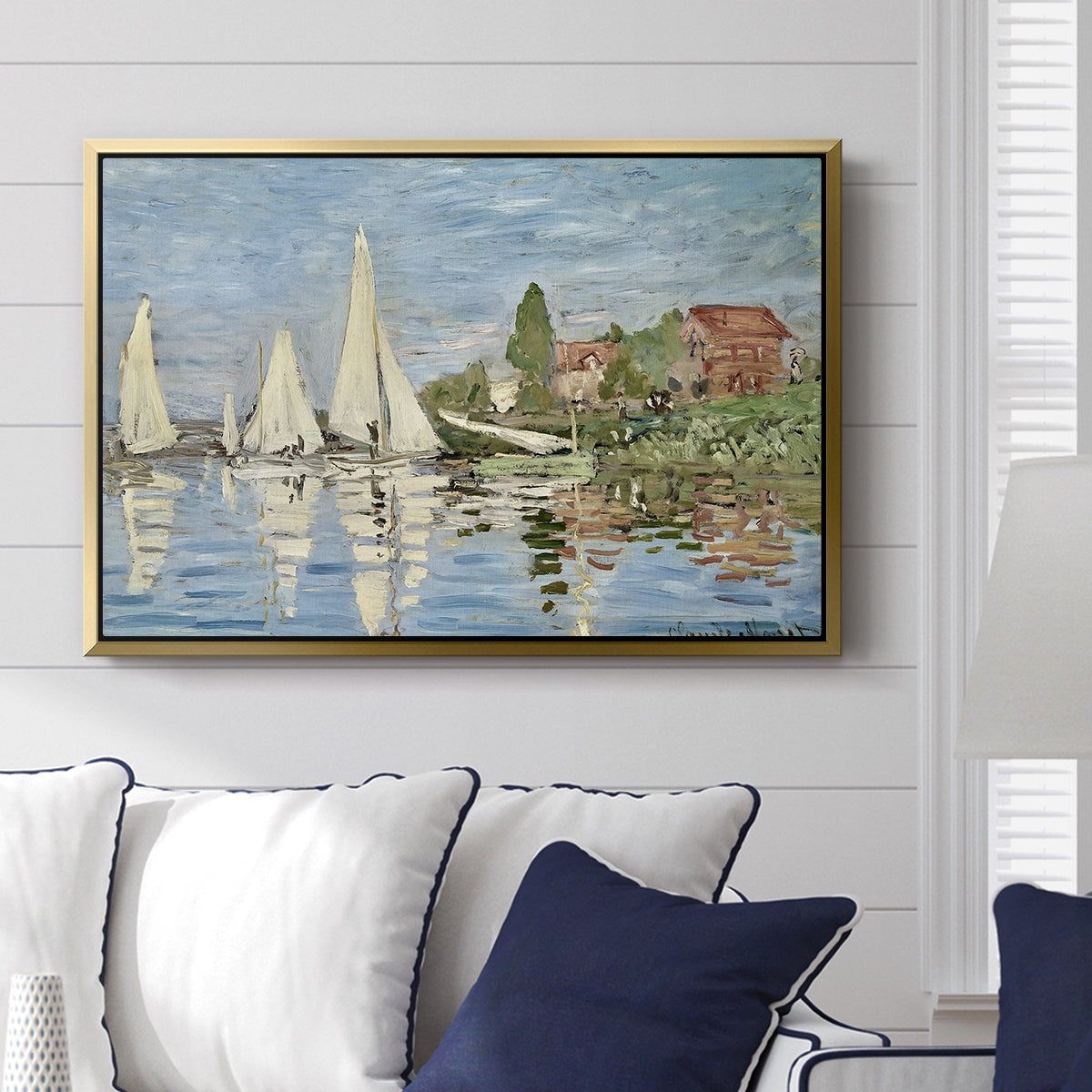 Regatta at Argenteuil, 1872 by Claude Monet displayed above a sofa in a living room in a gold floater frame, featuring a lively regatta scene with multiple boats and fluttering sails.