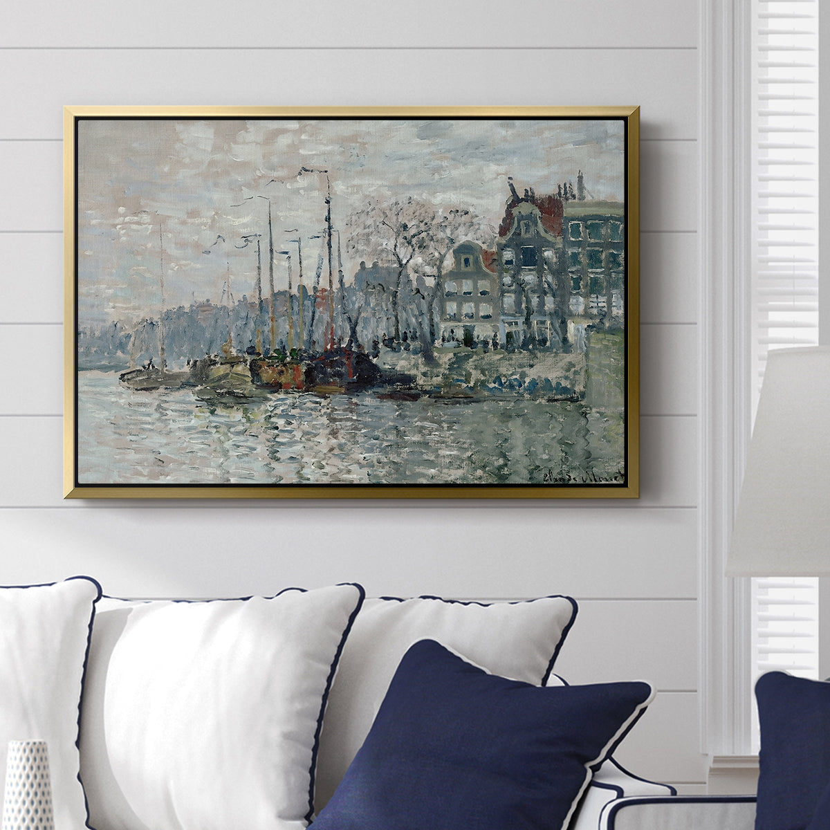 View of the Prins Hendrikkade and Kromme Waal in Amsterdam, 1874 by Claude Monet displayed above a sofa in a living room in a gold floater frame, featuring an impressionist cityscape of canal with ships and architecture.