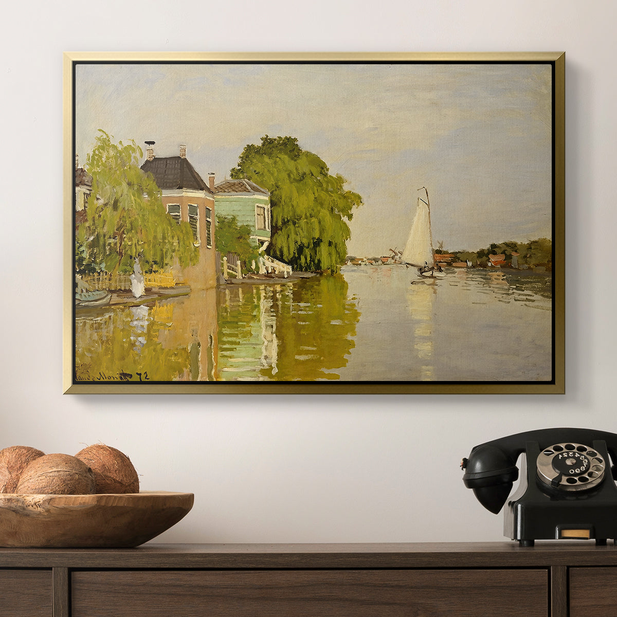Houses on the Achterzaan, 1871 by Claude Monet in a gold floater framed canvas displayed above a console table in a hallway, featuring a peaceful village scene with houses bordering water.