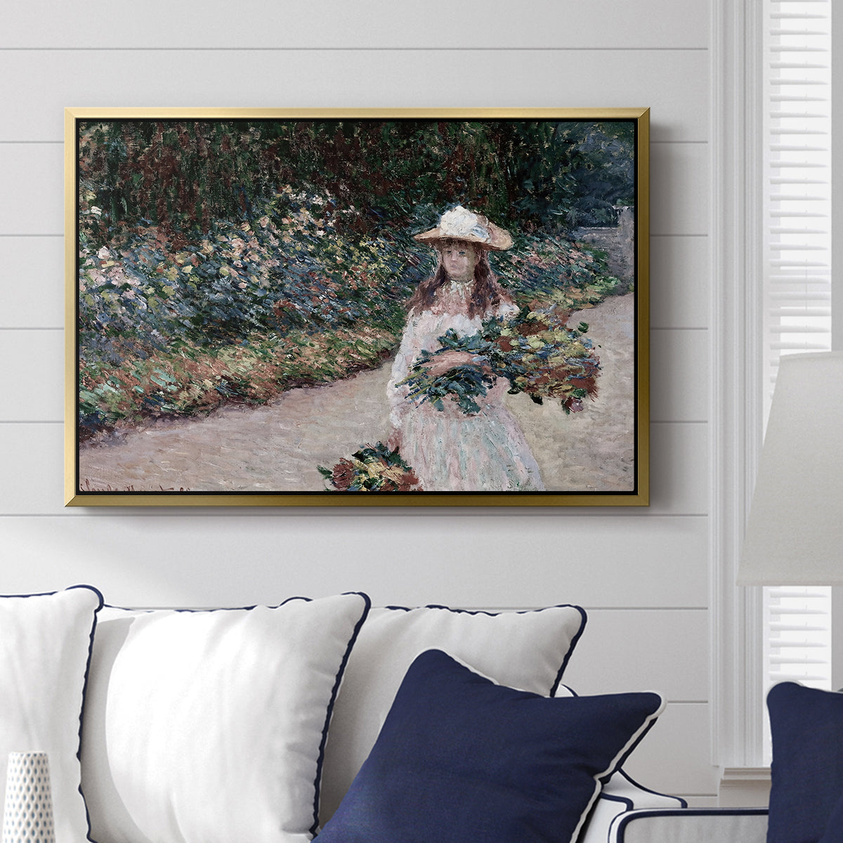 Young Girl in the Garden at Giverny, 1888 by Claude Monet displayed above a sofa in a living room in a gold floater frame, featuring an impressionist garden scene with child among greenery and blossoms.