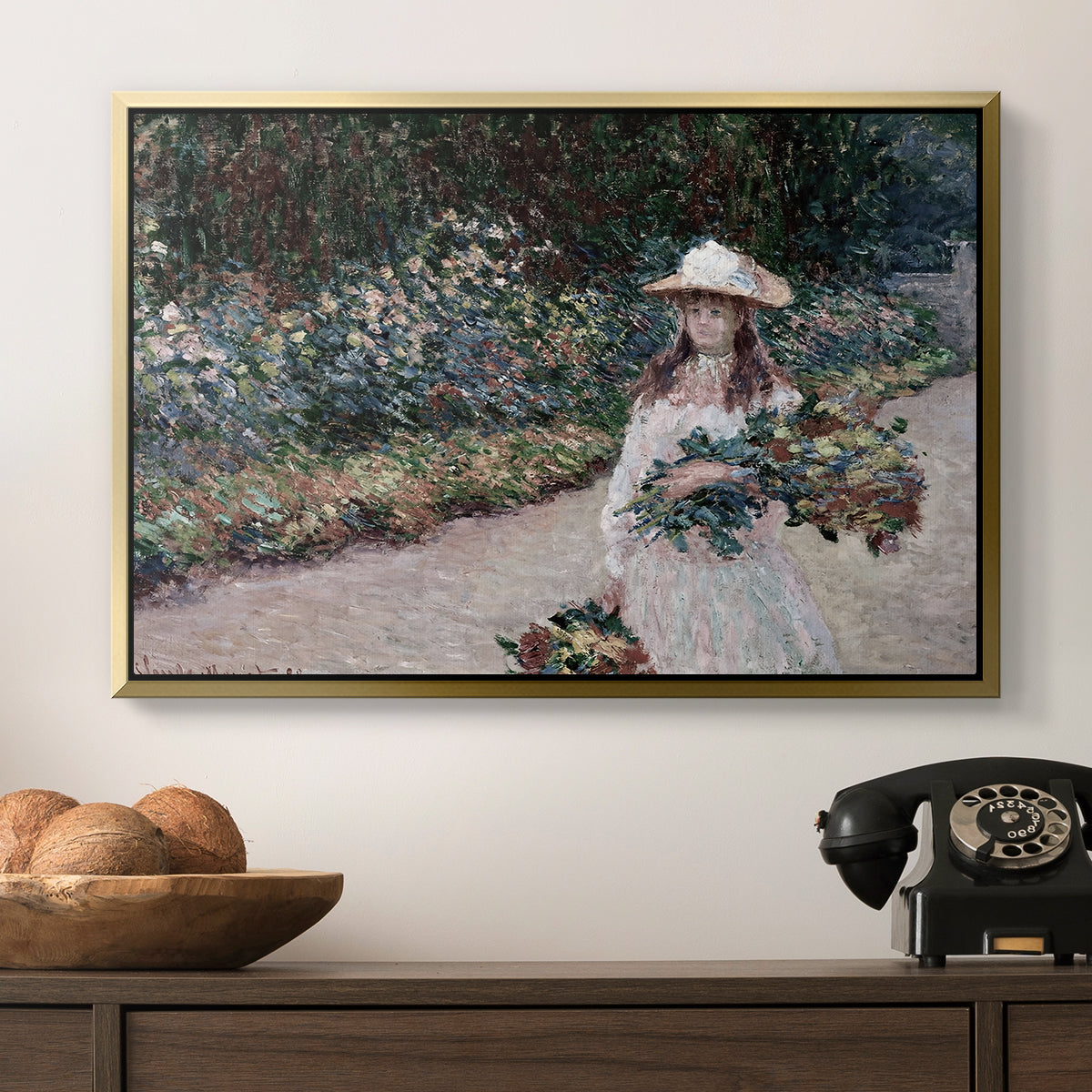 Young Girl in the Garden at Giverny, 1888 by Claude Monet in a gold floater framed canvas displayed above a console table in a hallway, featuring a tranquil outdoor portrait of girl in floral setting.
